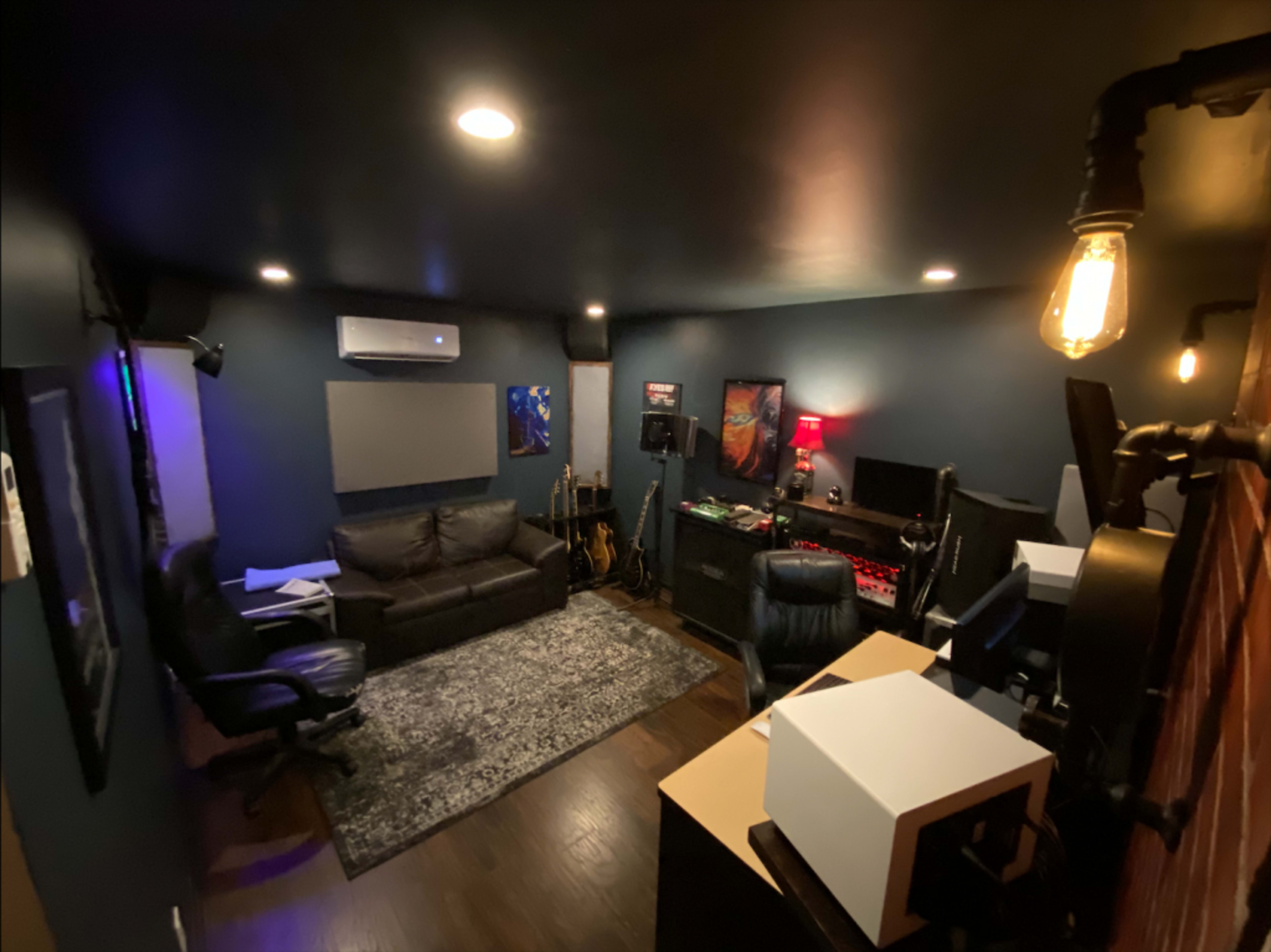 A dimly lit room designed for music or video production, featuring a couch, various instruments, and multiple workstations with computer equipment.