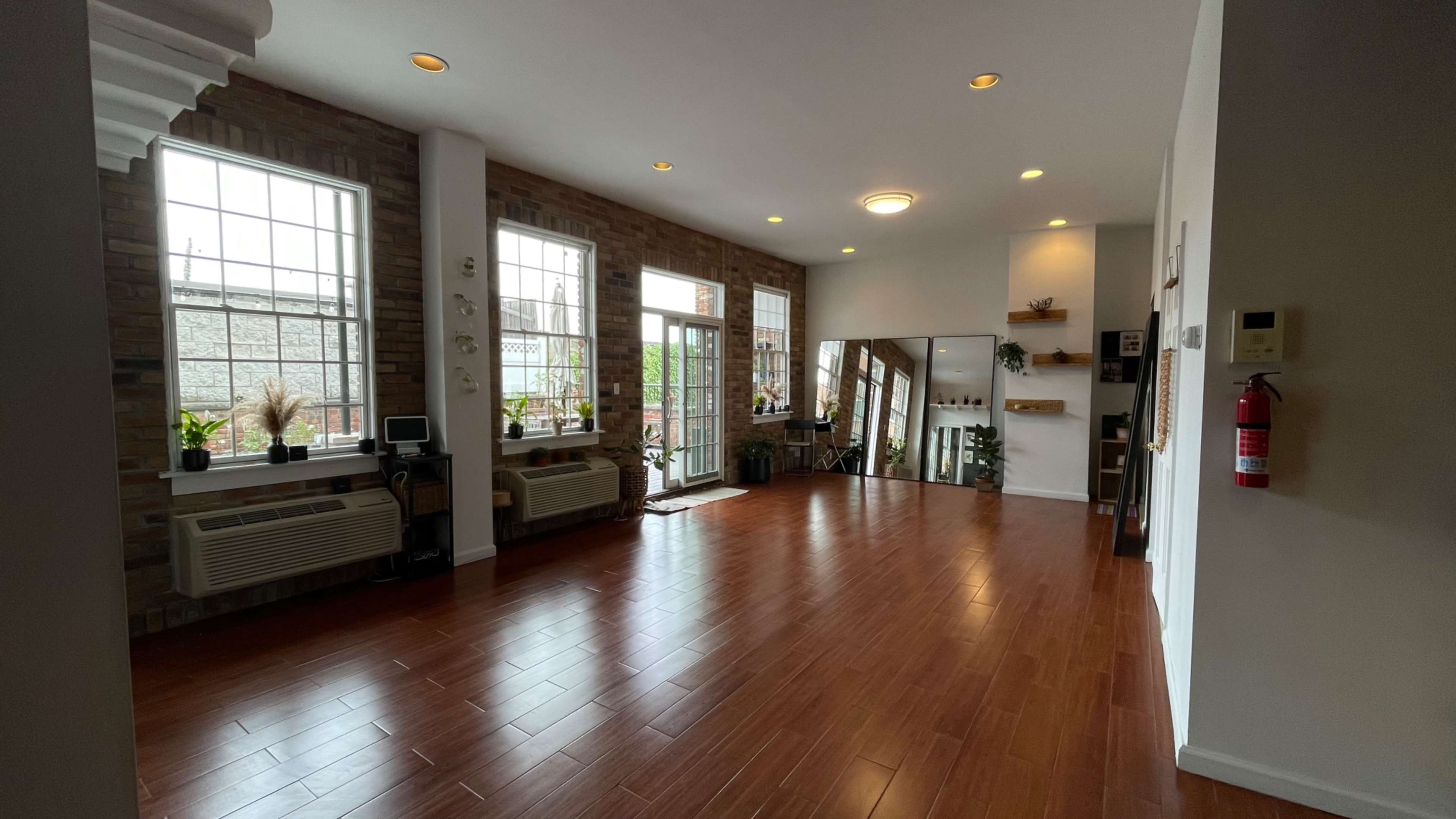 A spacious interior room with large windows, wooden flooring, and a minimalist decor featuring plants and furniture.