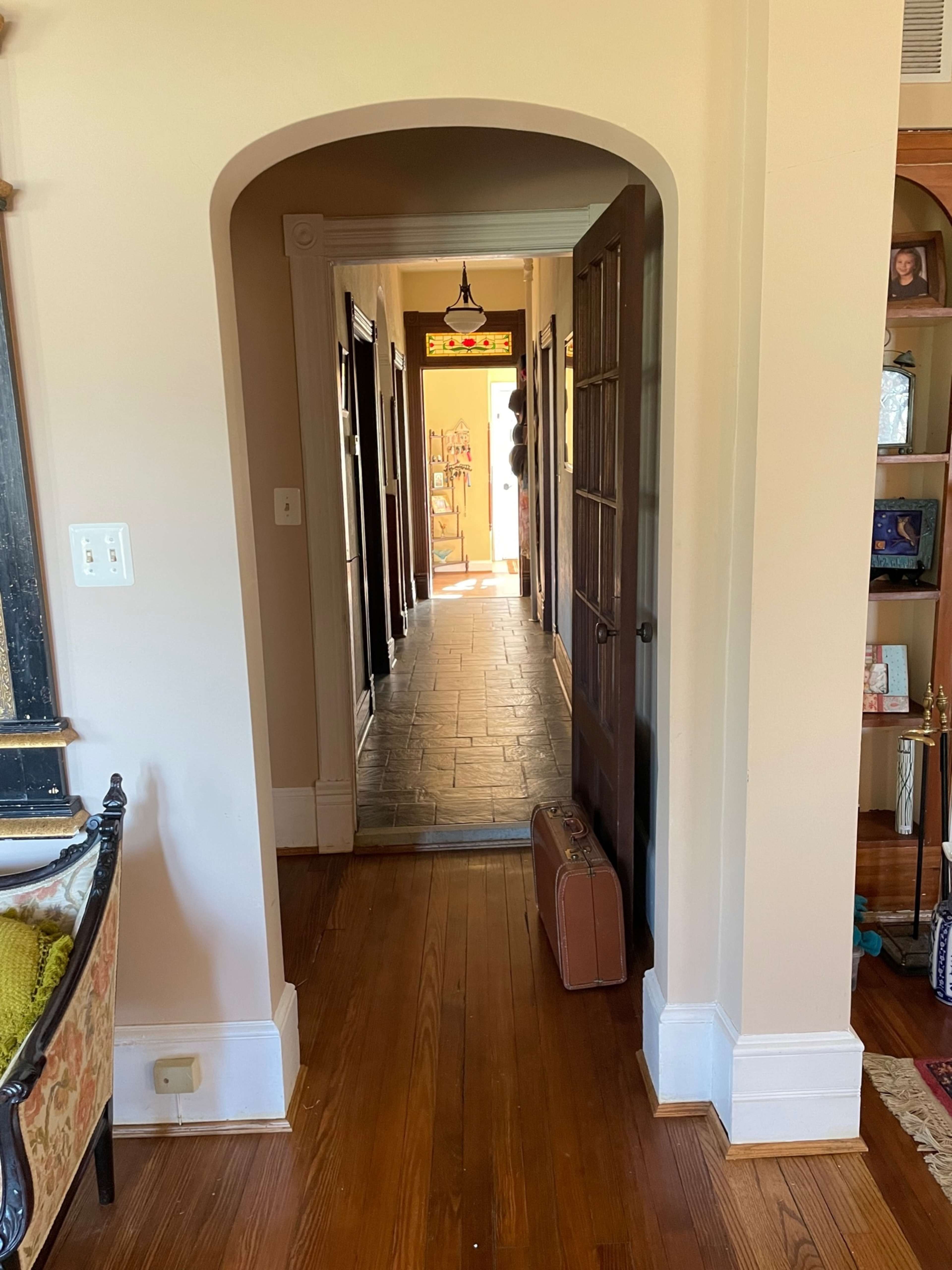 A long hallway with door openings on either side and a suitcase placed on the wooden floor near the entrance.