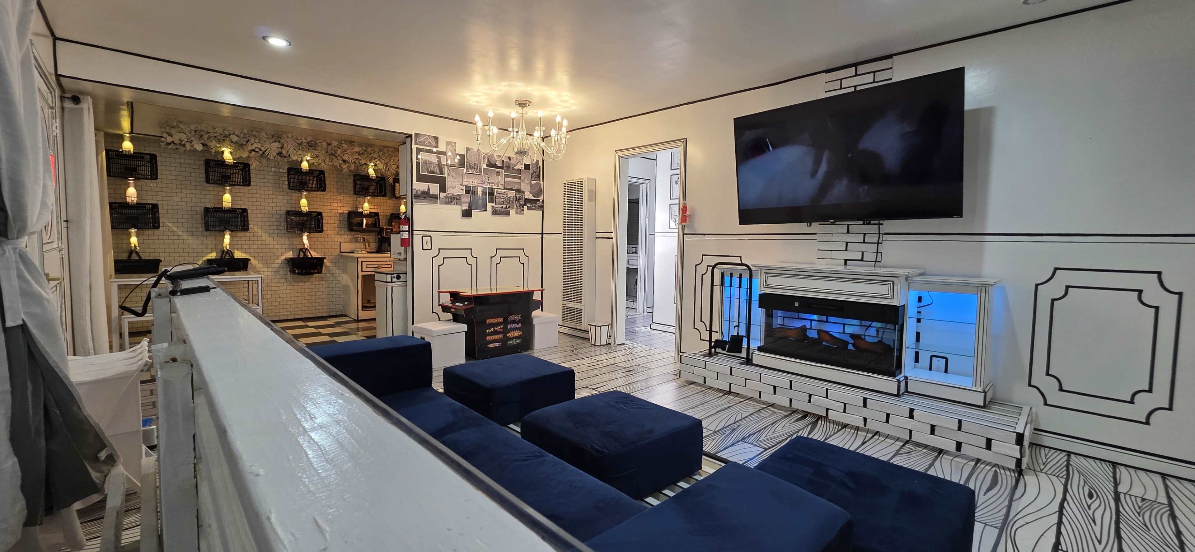 The image shows a modern living room with a fireplace, a large television mounted on the wall, and blue seating arranged around a patterned floor.