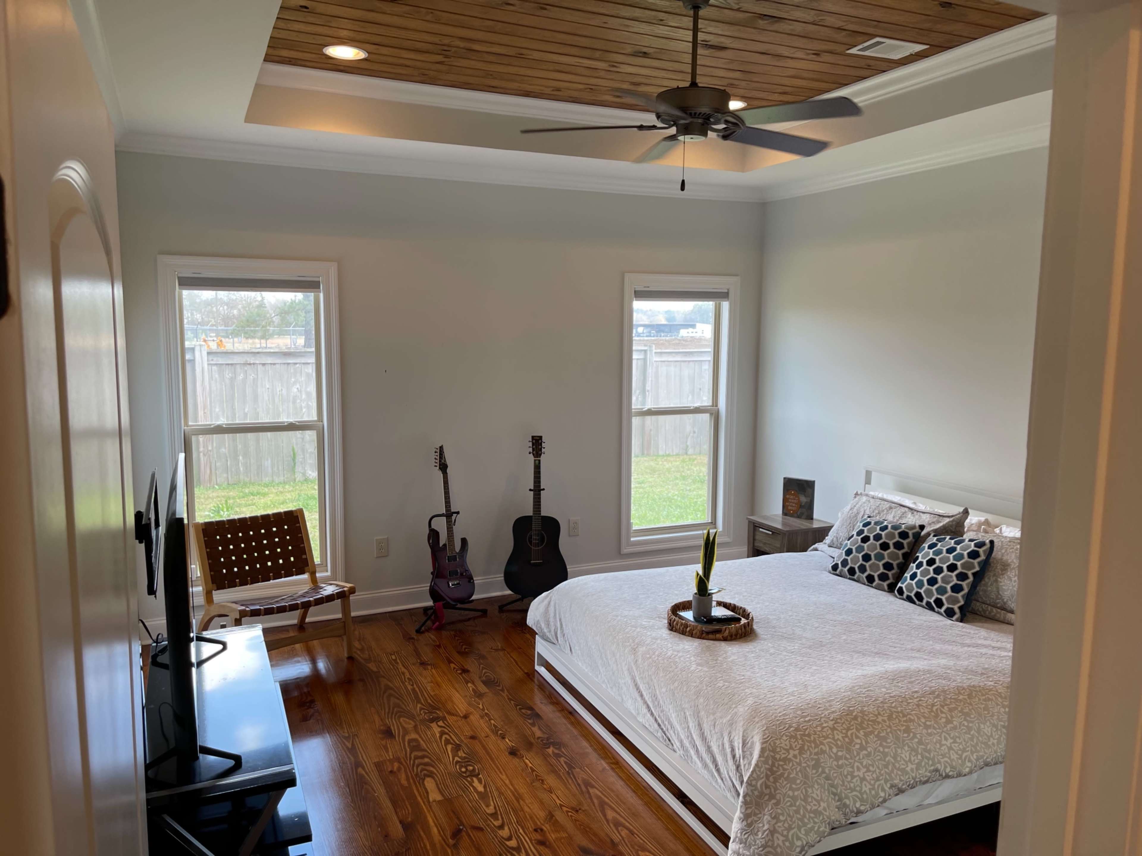 A bedroom featuring a large white bed, two windows, a wooden ceiling, and a couple of guitars leaning against the wall.