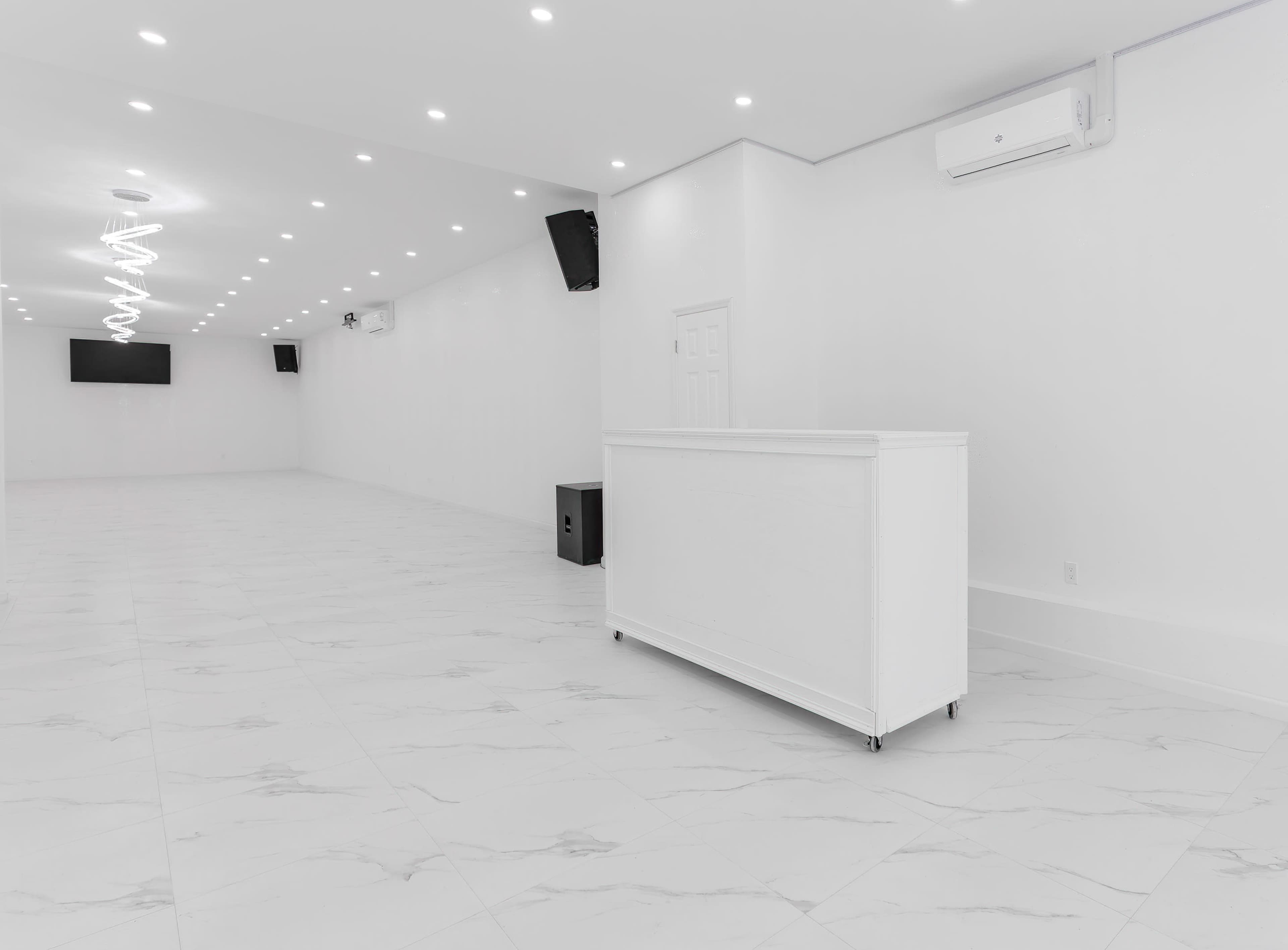 A large, empty room with white walls, white tile flooring, and a white reception desk against one wall.