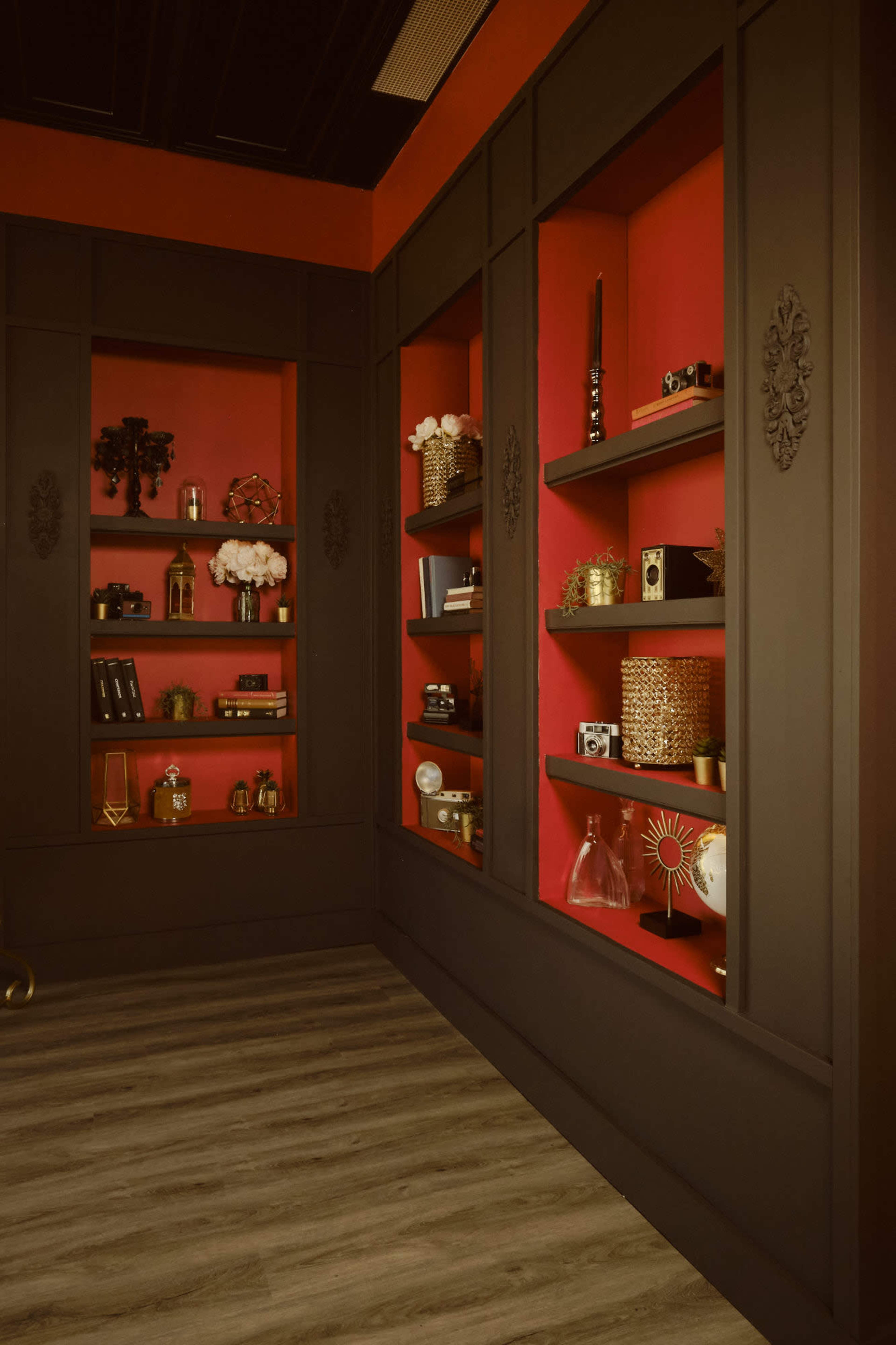 The image shows a stylish interior featuring dark cabinets with shelves filled with decorative items against a vibrant red wall.
