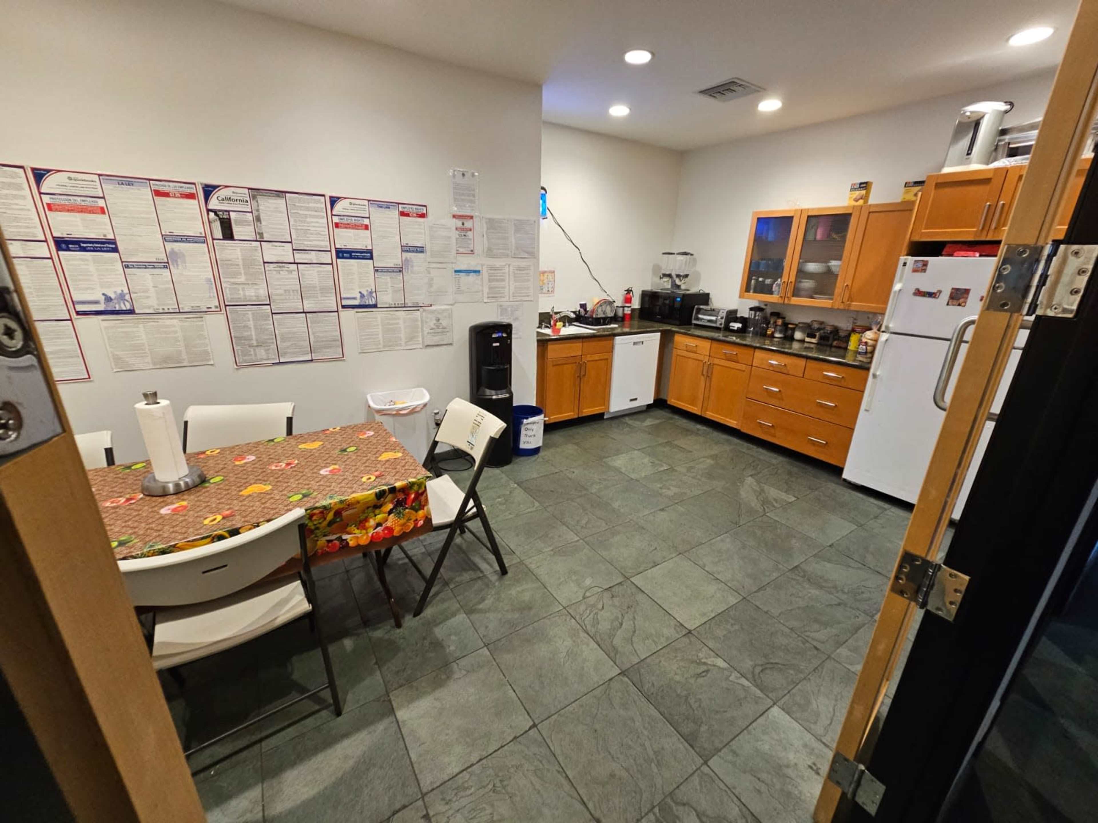 A kitchen with a table and chairs, cabinetry, appliances, and various posters or notices on the wall.