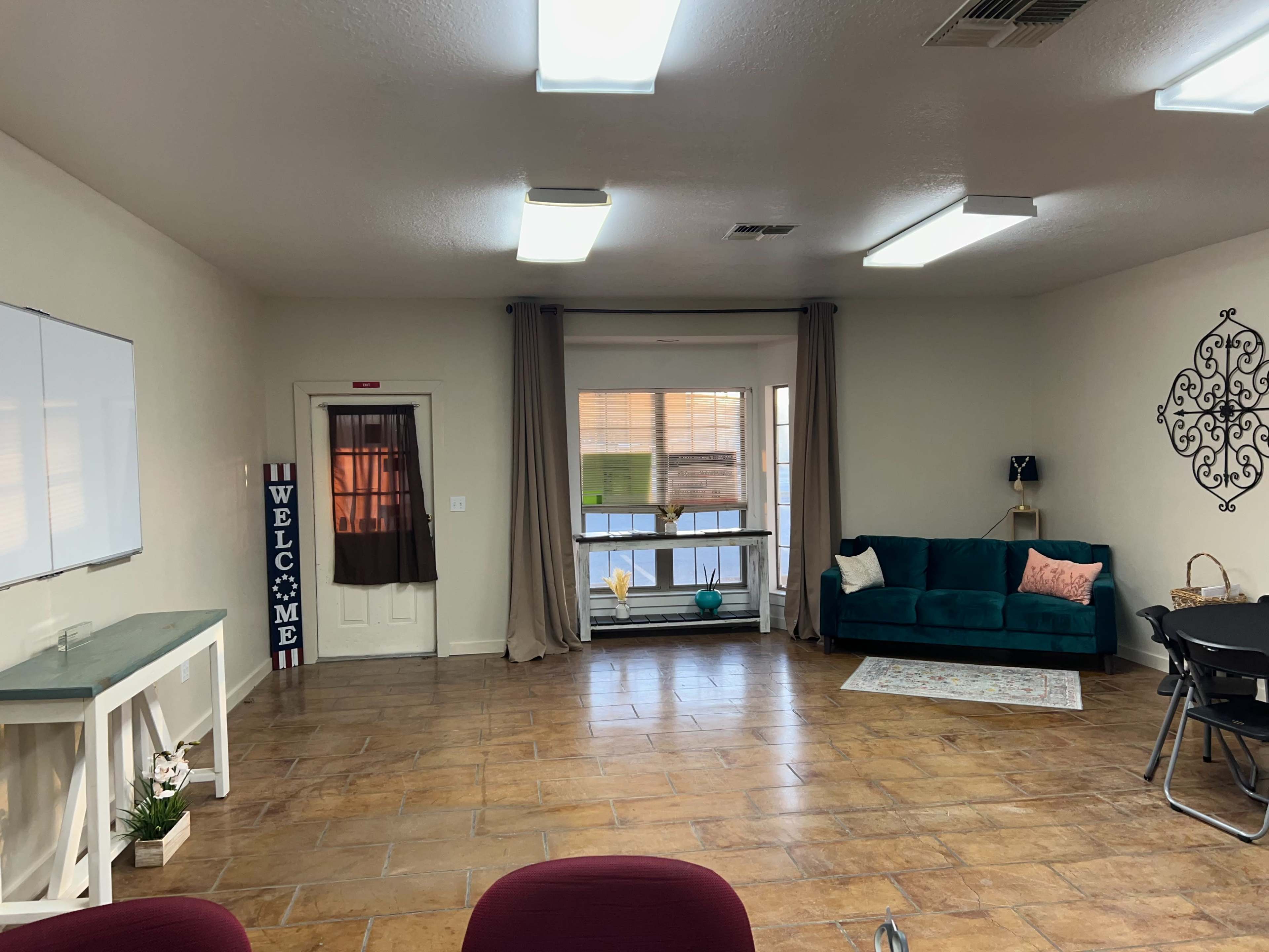 A spacious room with a seating area, a whiteboard on the wall, and large windows partially covered by curtains.