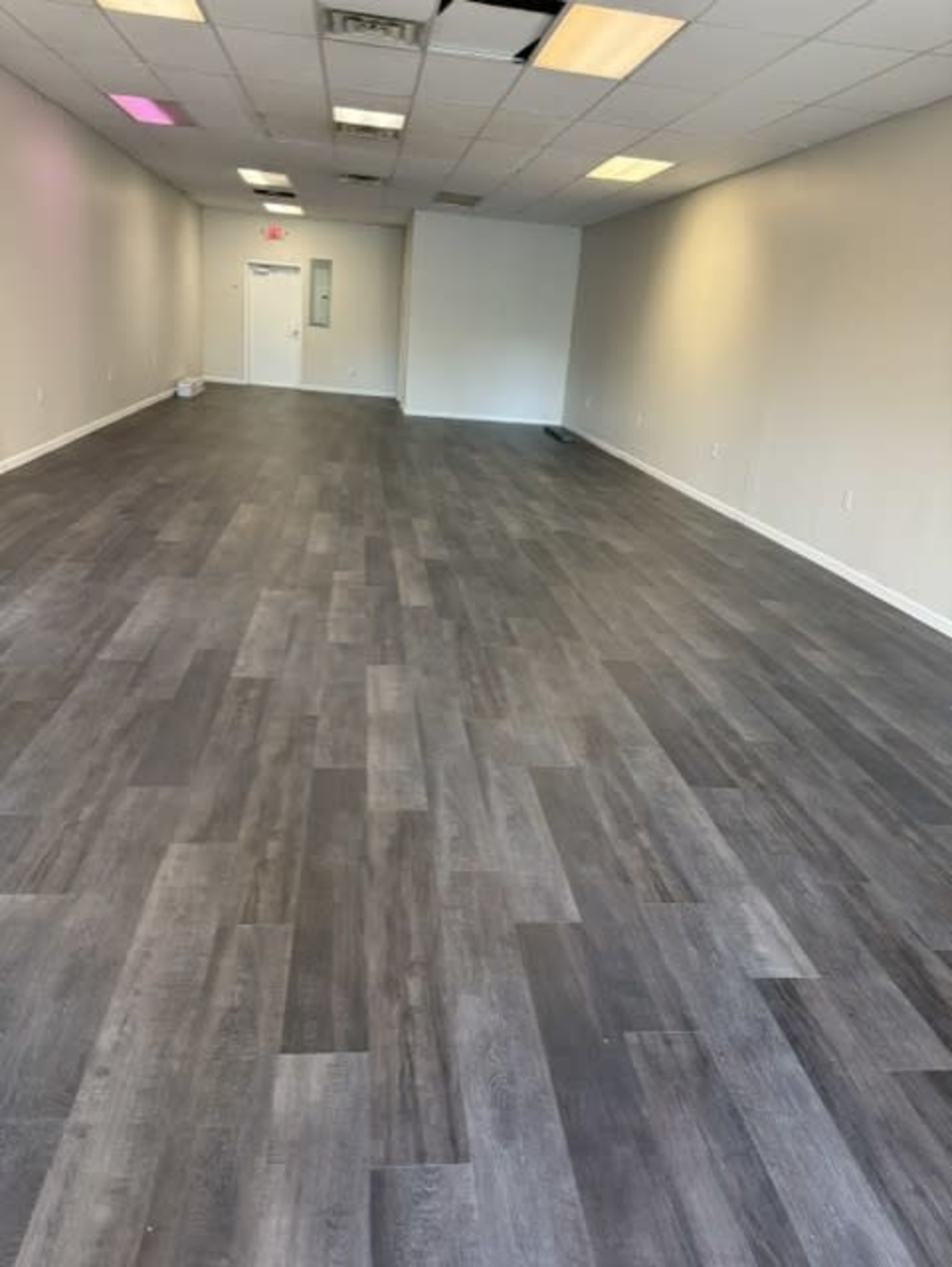 The image shows an empty interior space with gray laminate flooring and light-colored walls.