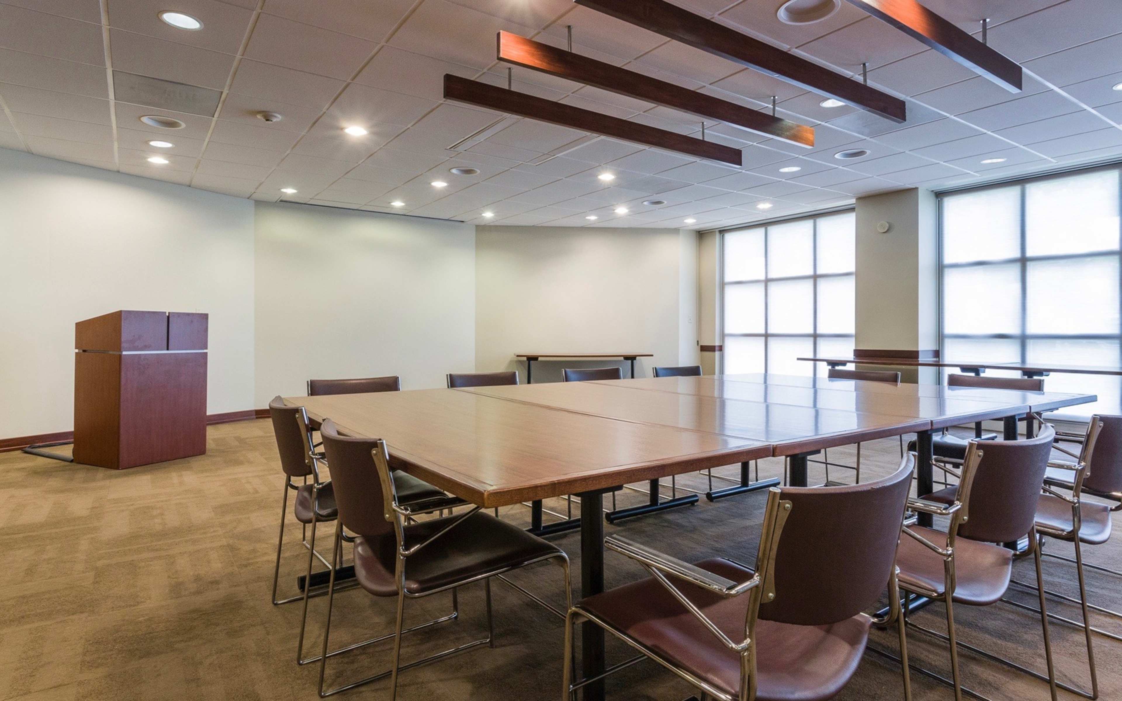 A spacious, well-lit meeting room with a large rectangular table surrounded by chairs and a podium in one corner.