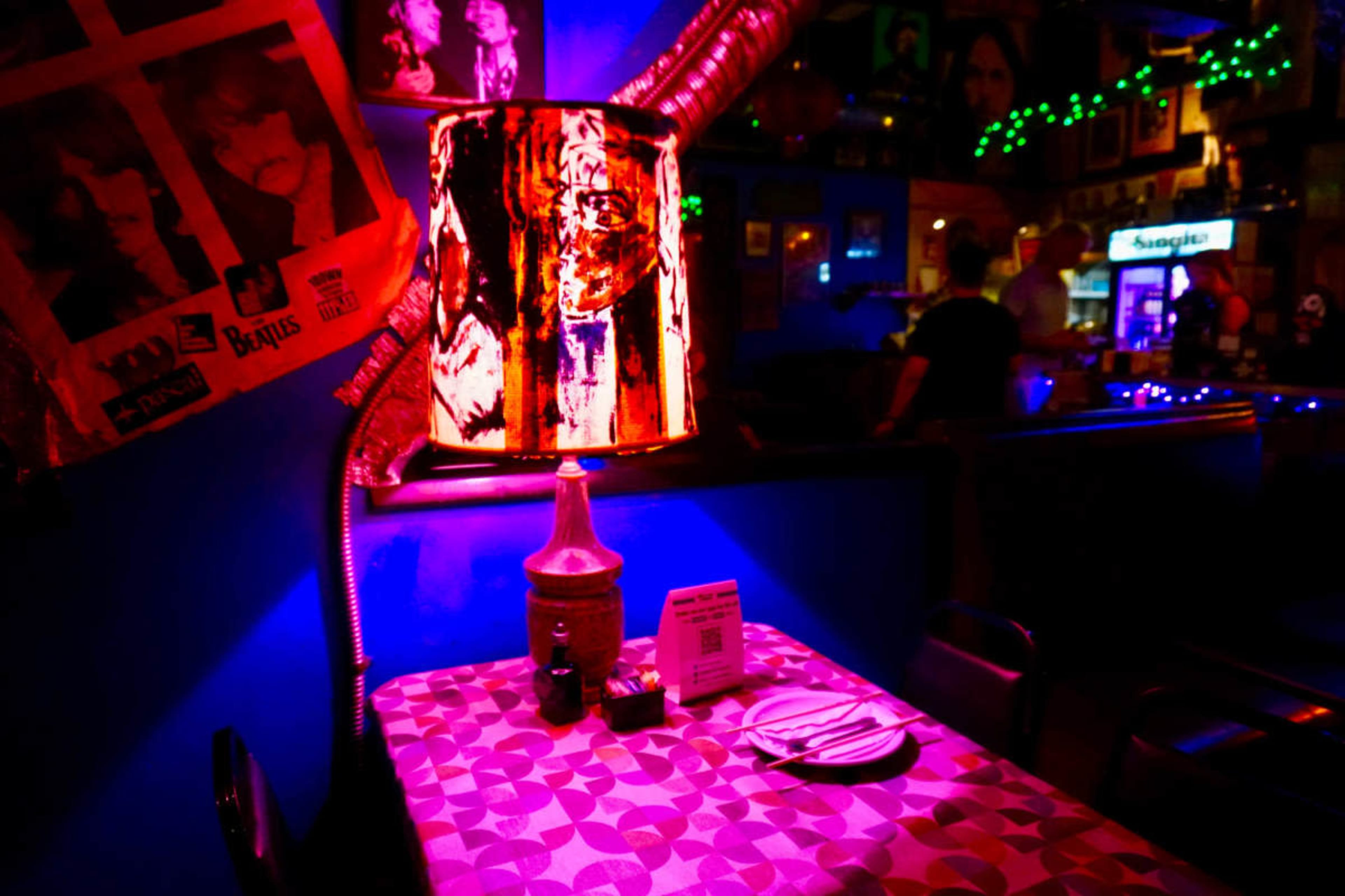 A table with a lamp and condiments is set in a dimly lit bar decorated with music memorabilia.
