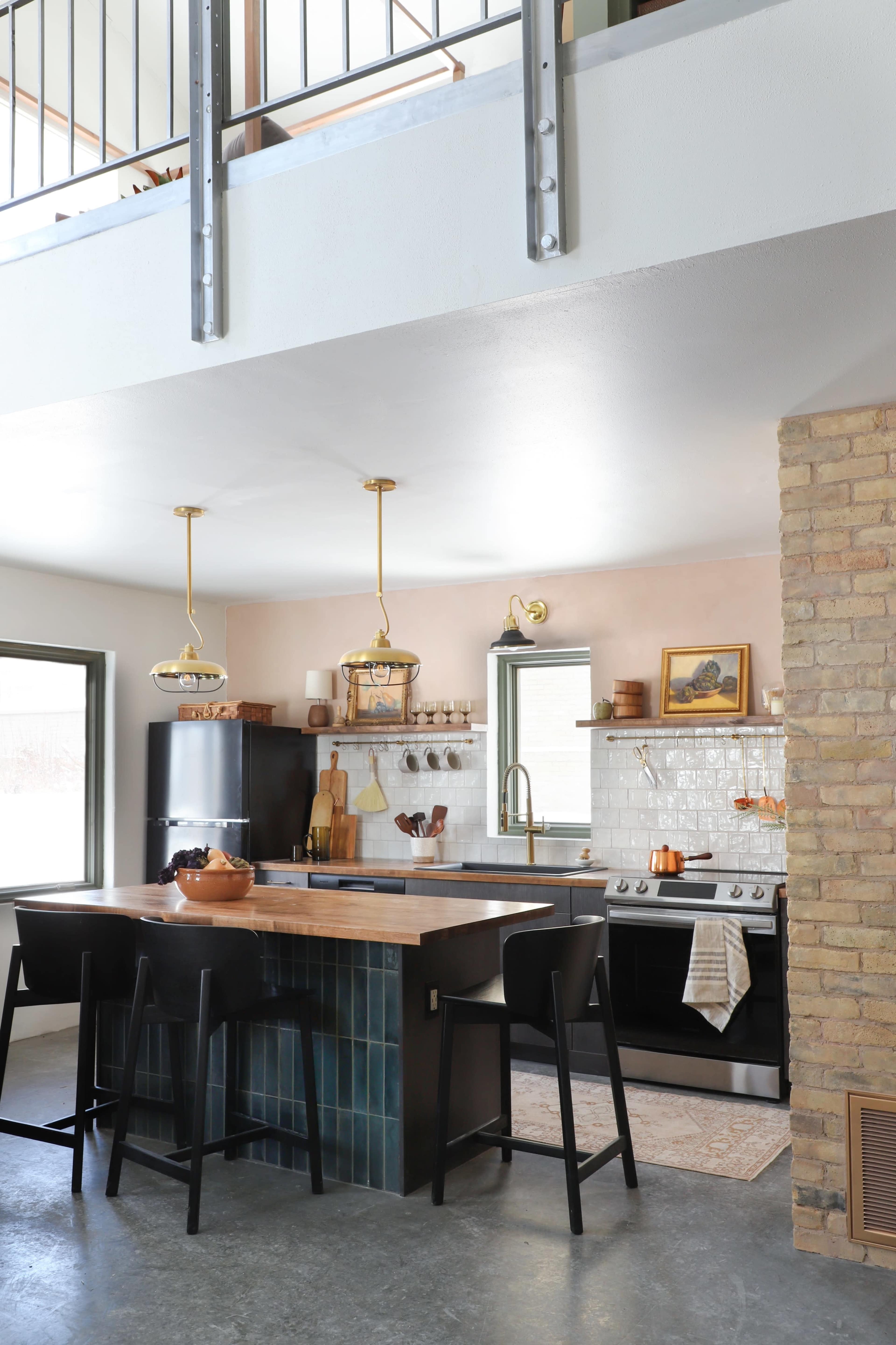 A modern kitchen with a central island featuring black stools, stainless steel appliances, and light-colored cabinetry.