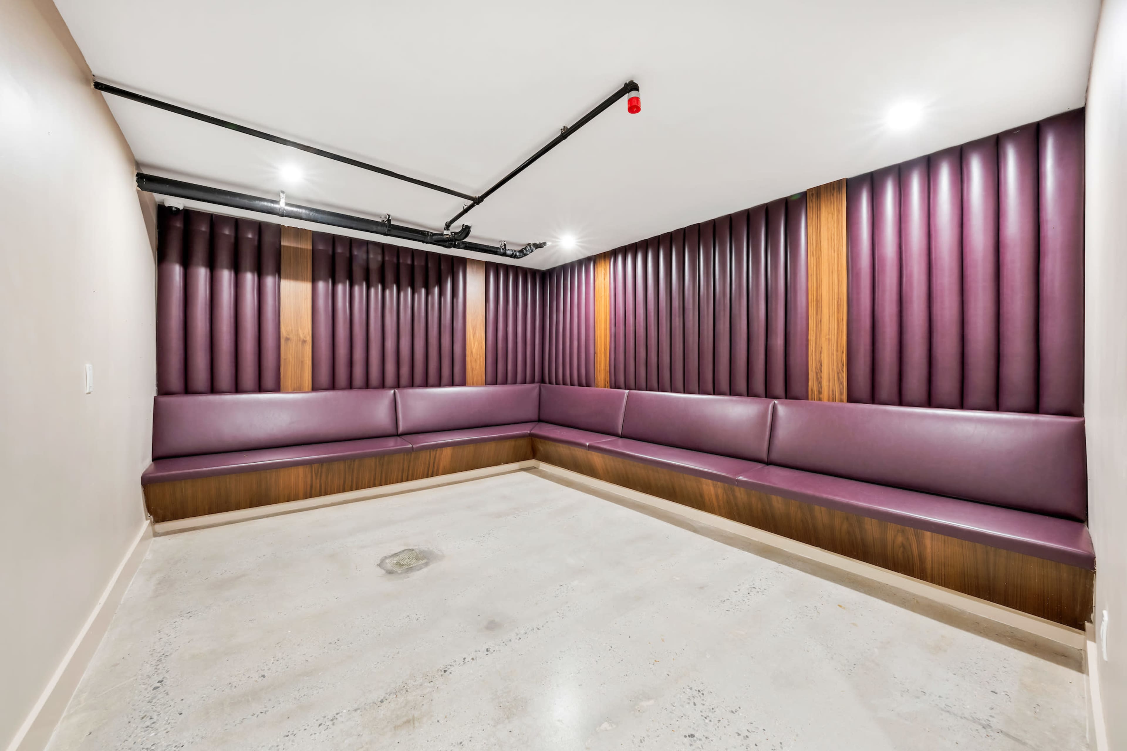 A small, modern room with purple upholstered walls and a curved wooden bench.