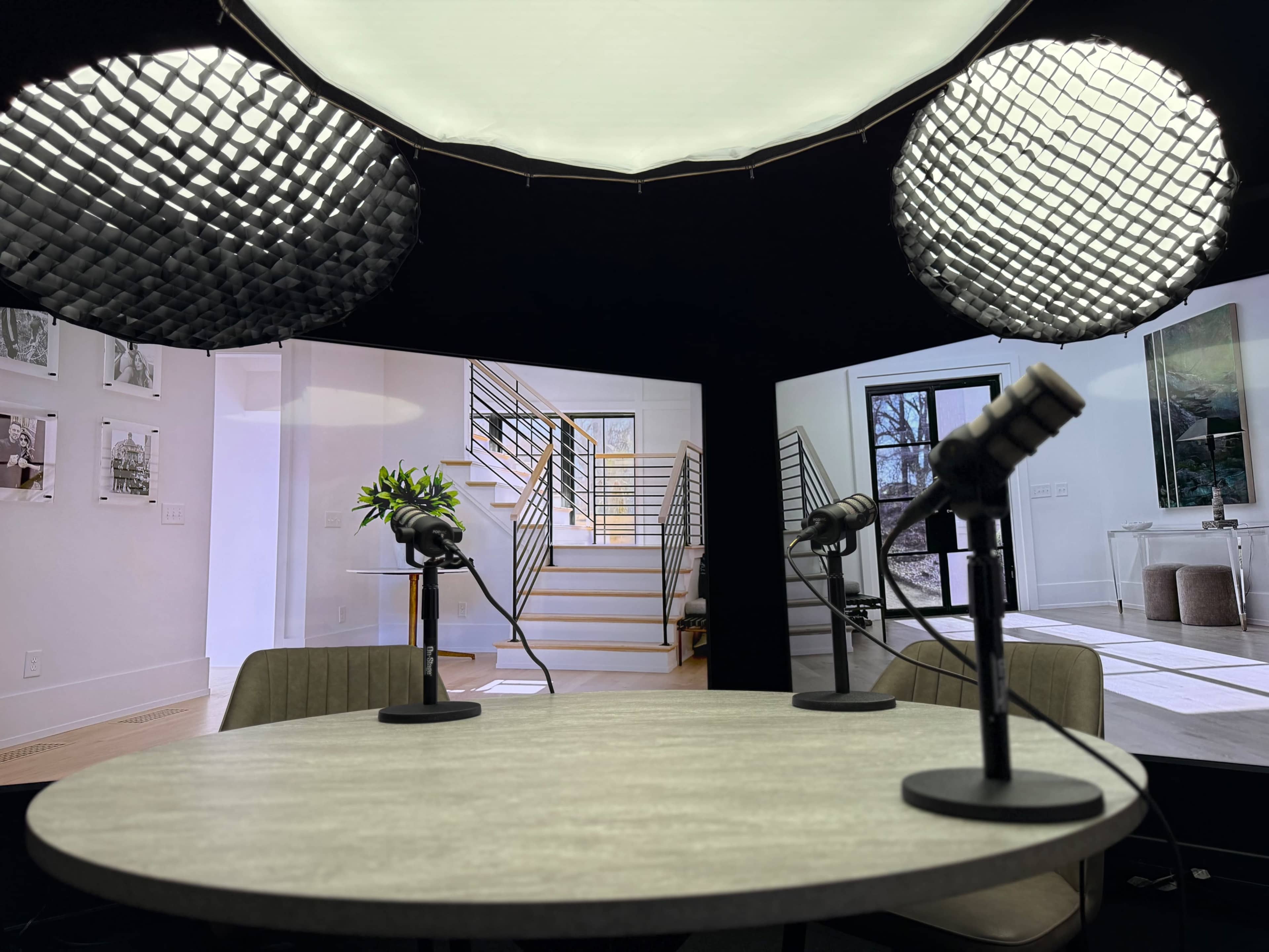 A circular table with microphones is set up in front of two large screens displaying images of modern interior spaces.