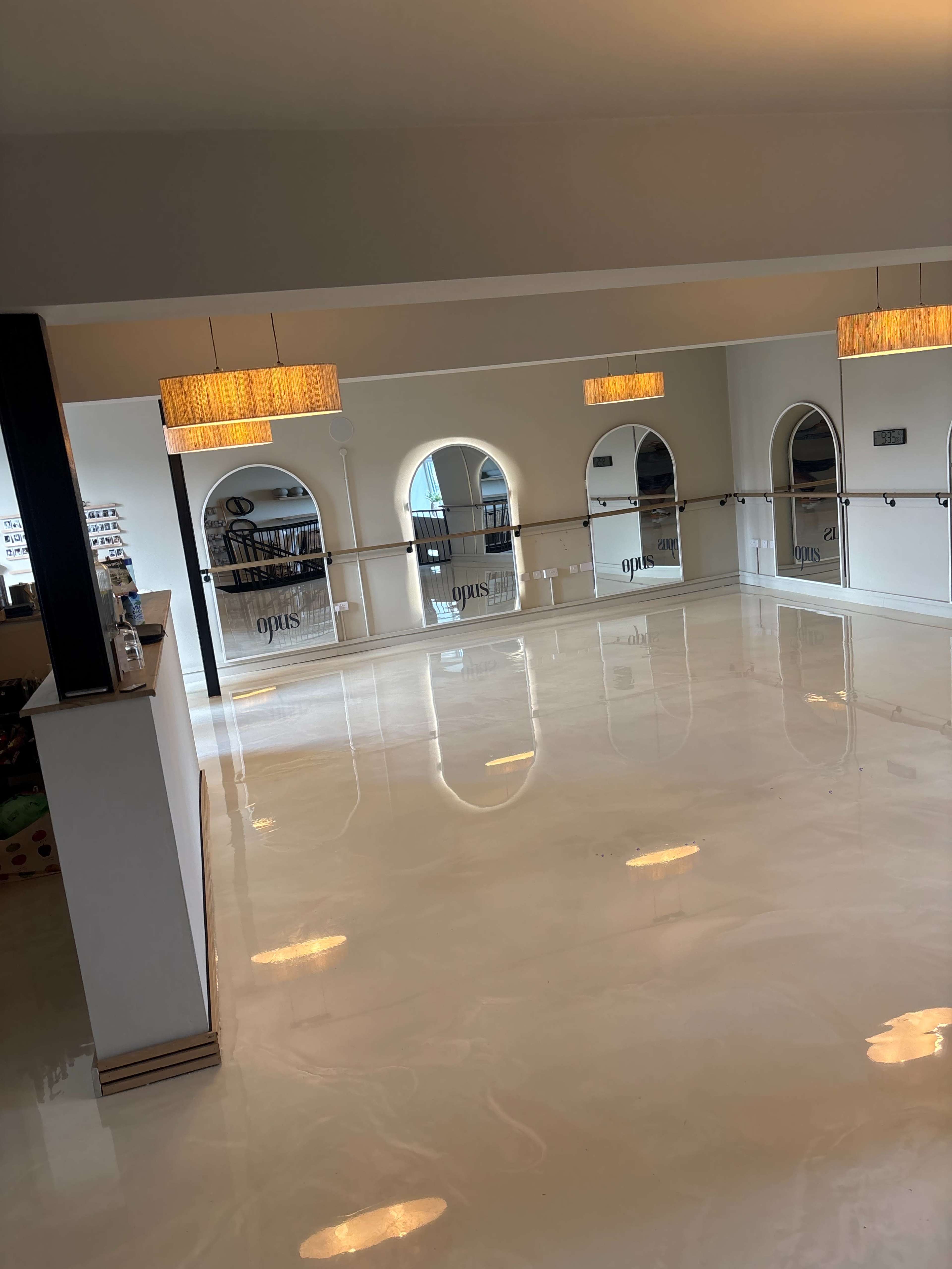 The image shows a spacious, empty dance studio with a glossy floor, large mirrors, and pendant lighting.