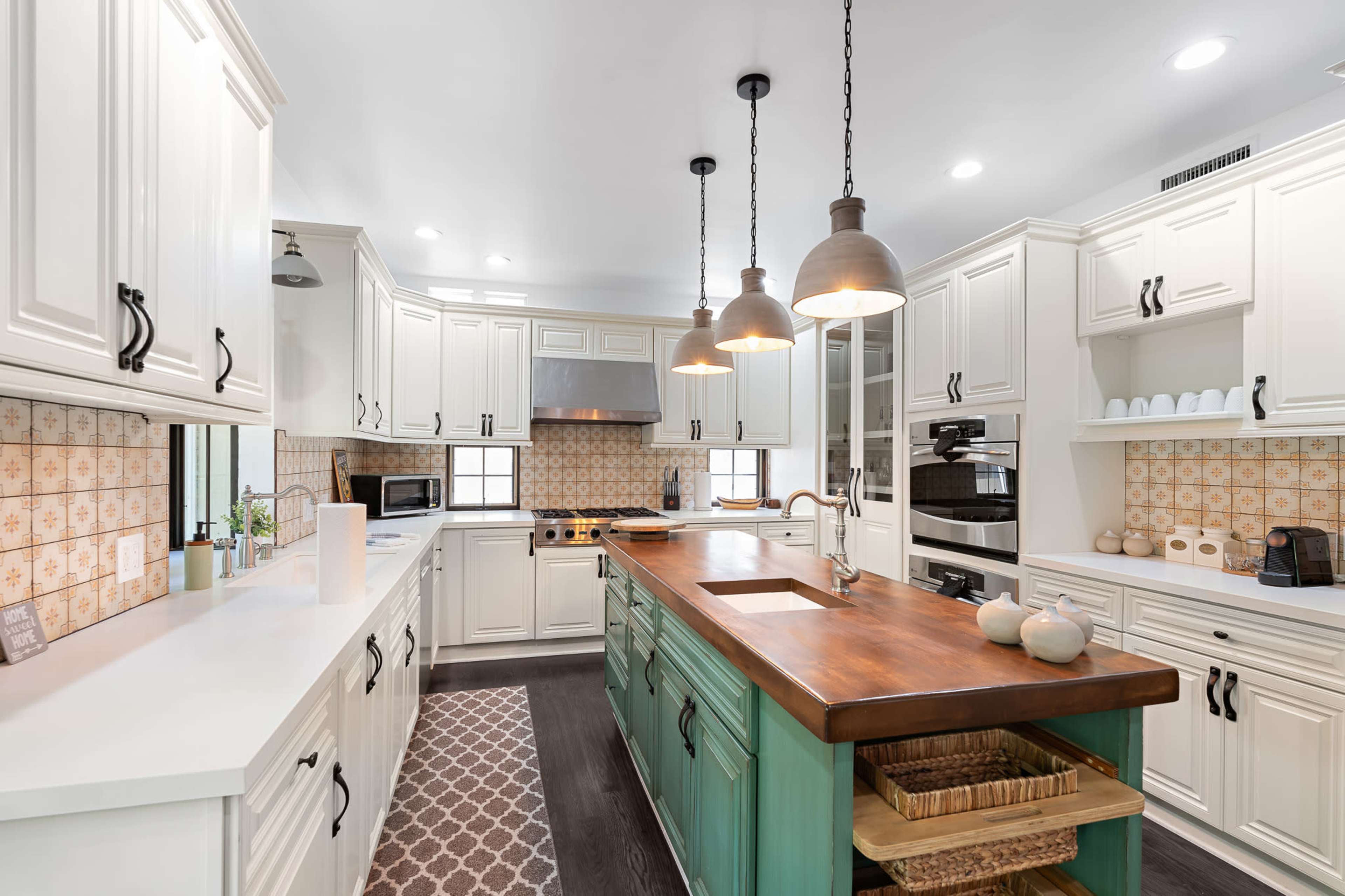 A modern kitchen with white cabinets, a central wooden island, and decorative tiles on the walls.