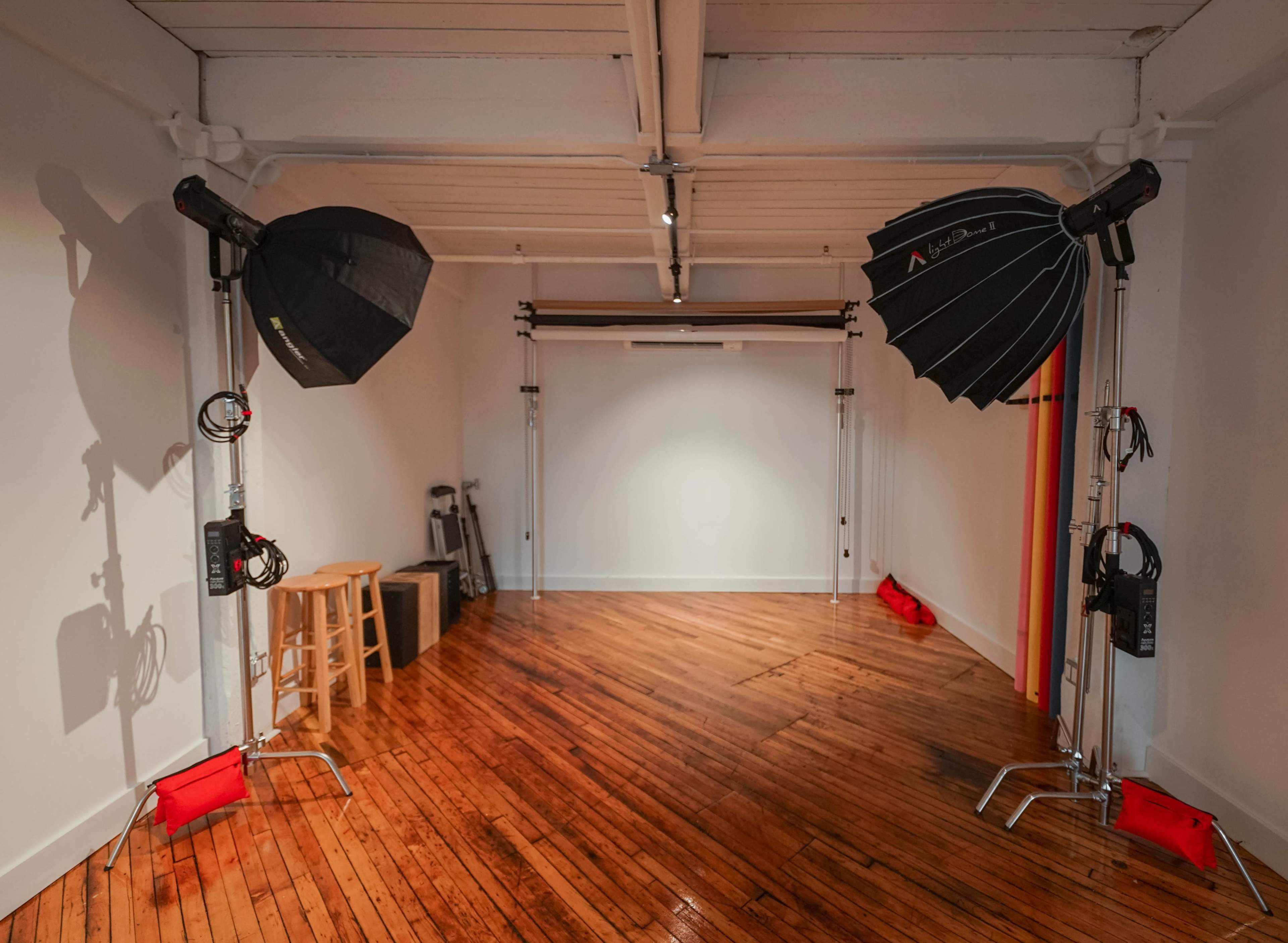 A photography studio features two large softbox lights on stands, a seamless backdrop setup, and polished wooden flooring.