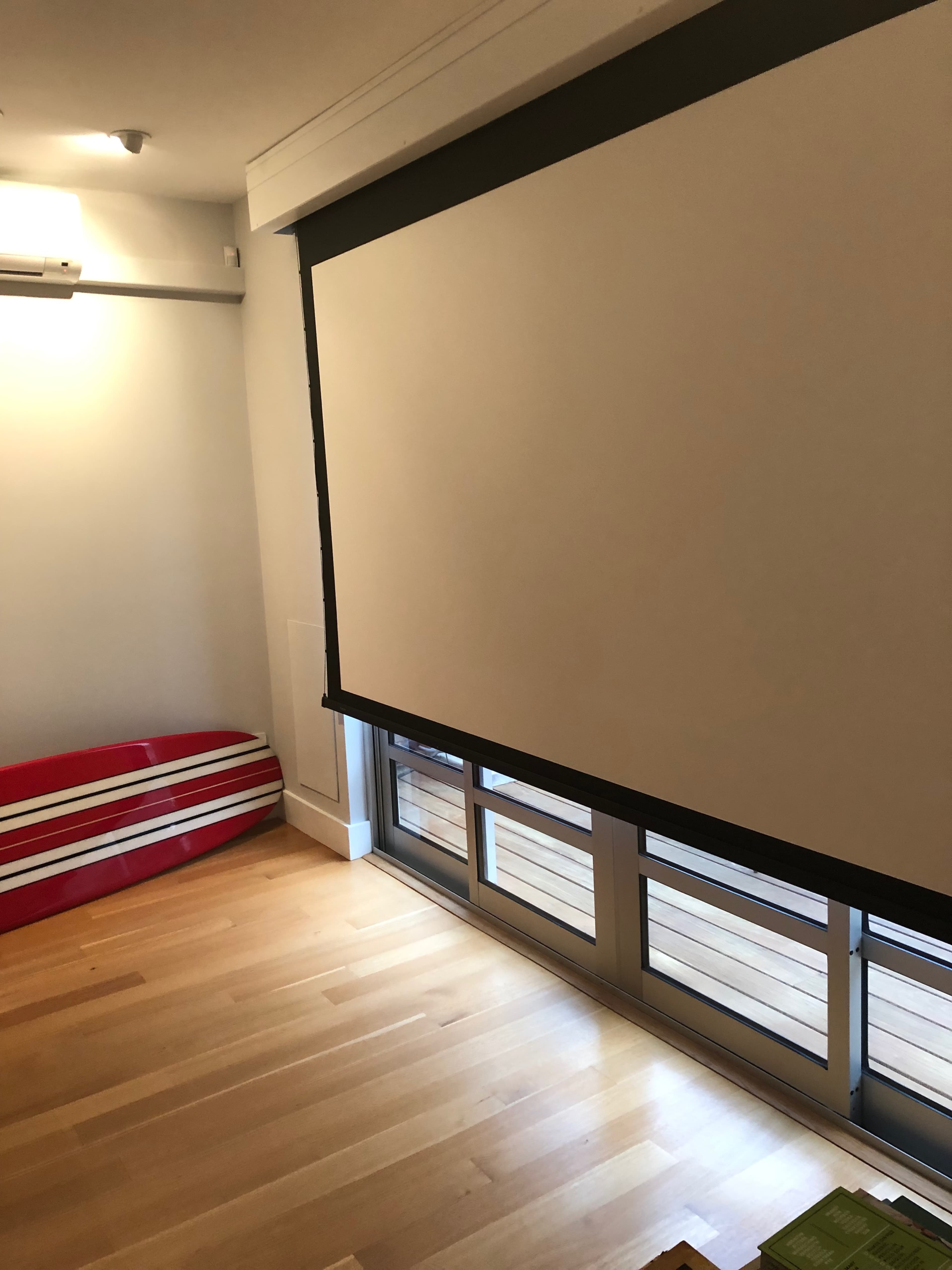 The image shows a room with a large retractable screen positioned near a window and a red striped object in the corner.