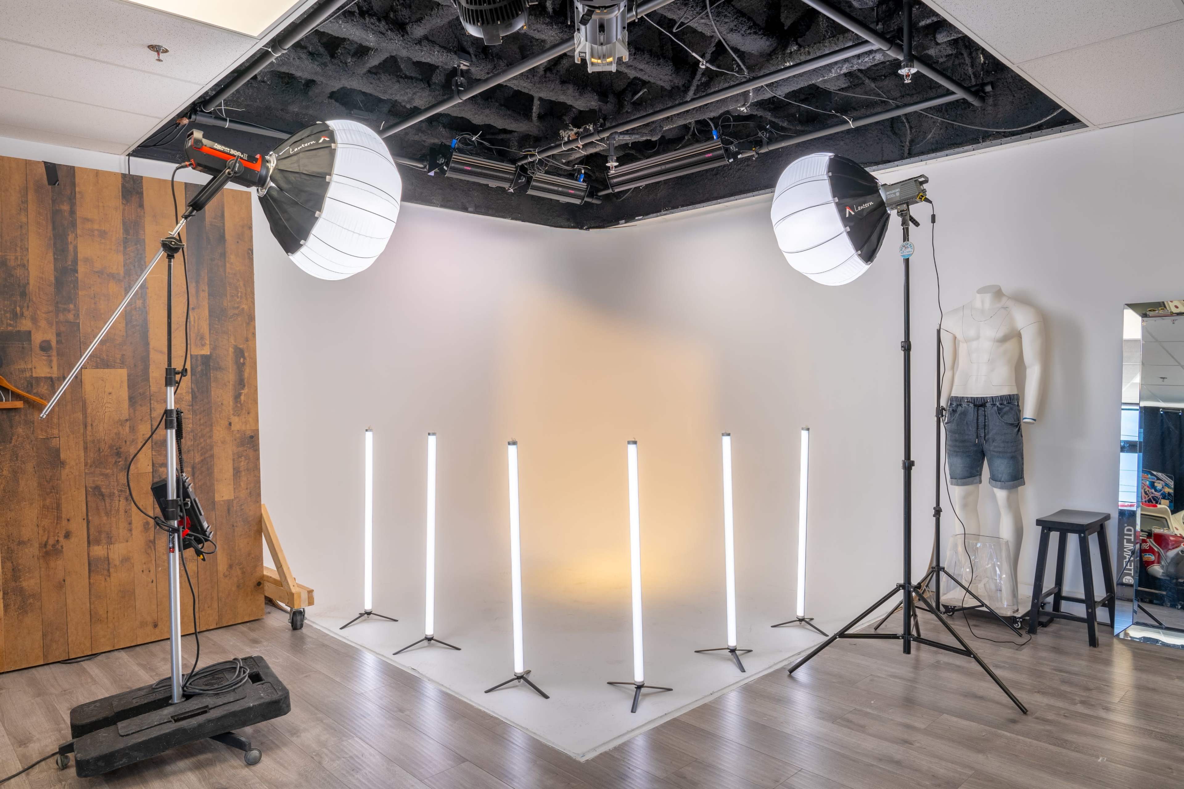 The image shows a photography studio with softbox lights and illuminated tall stands arranged in a semi-circle against a plain backdrop.
