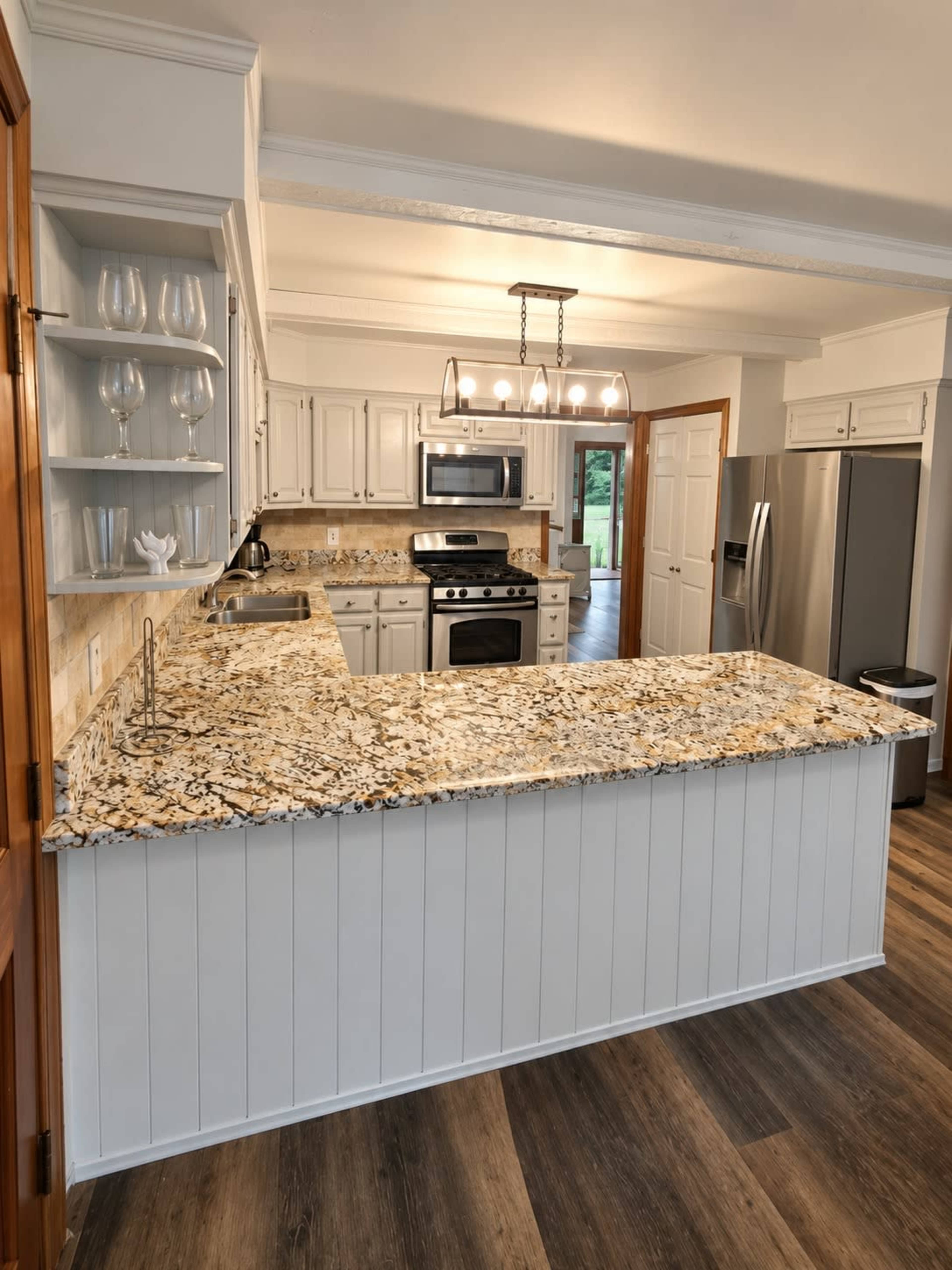 The image depicts a modern kitchen with light-colored cabinets, a granite countertop, stainless steel appliances, and a spacious layout.
