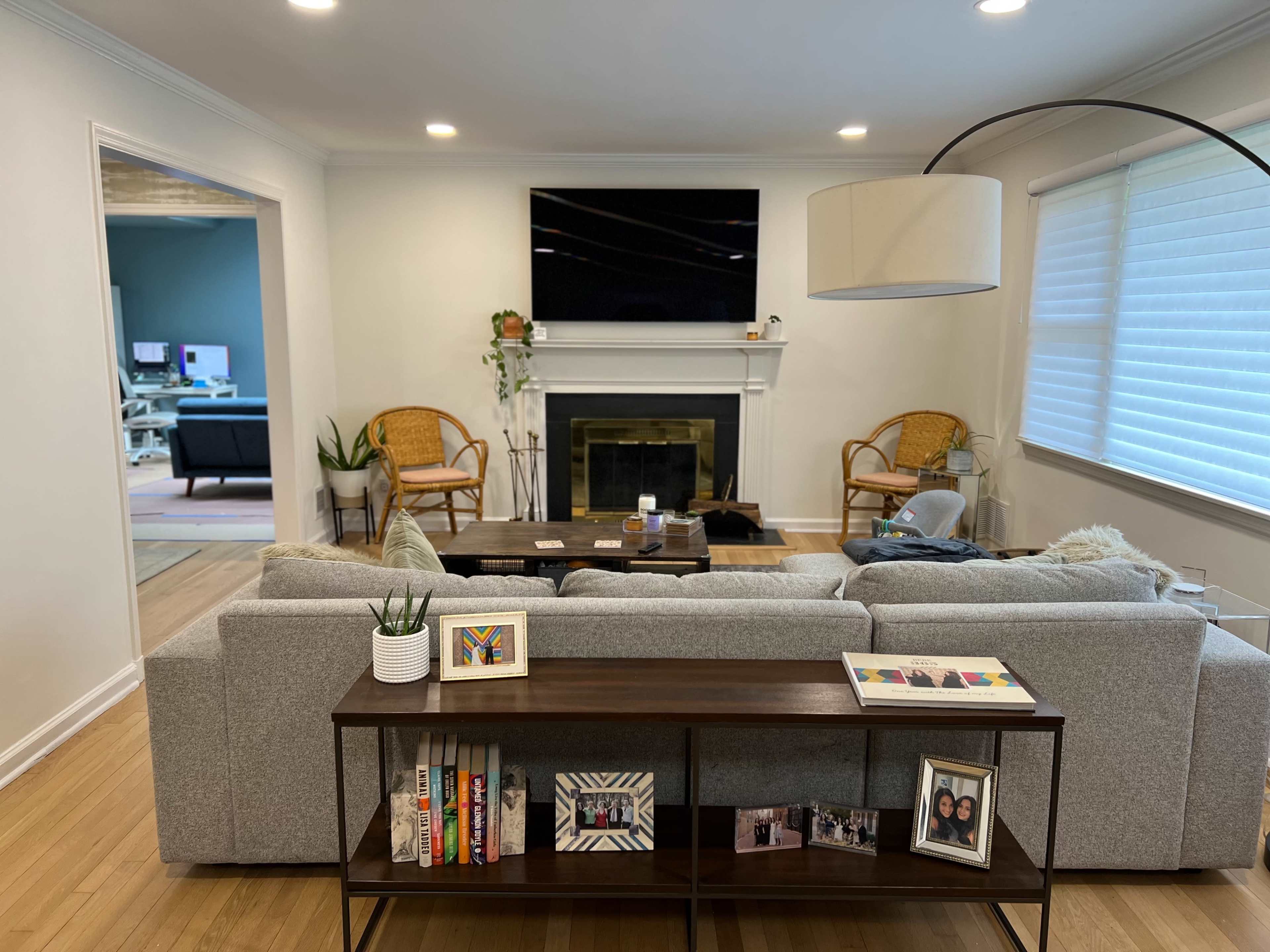 A modern living room features a gray sofa, a coffee table, and a television above a fireplace, with two rattan chairs on either side.