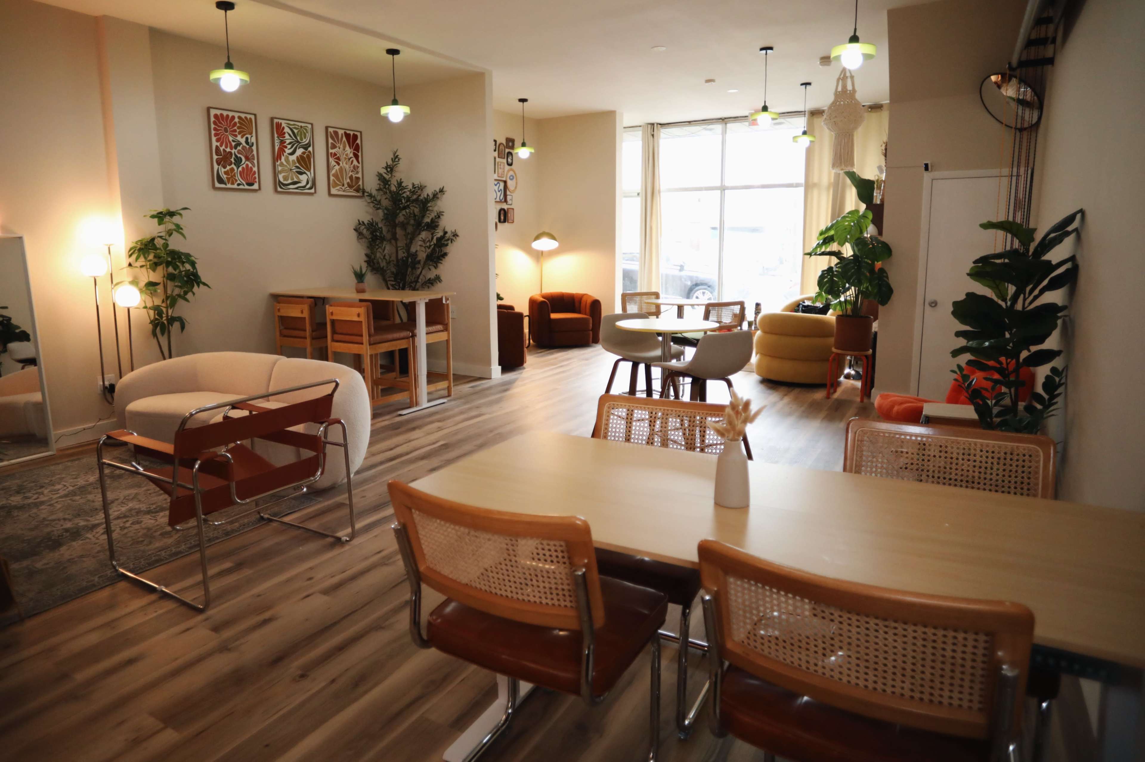The image shows a well-lit interior space with various seating arrangements, including a dining table, lounge chairs, and decorative plants.