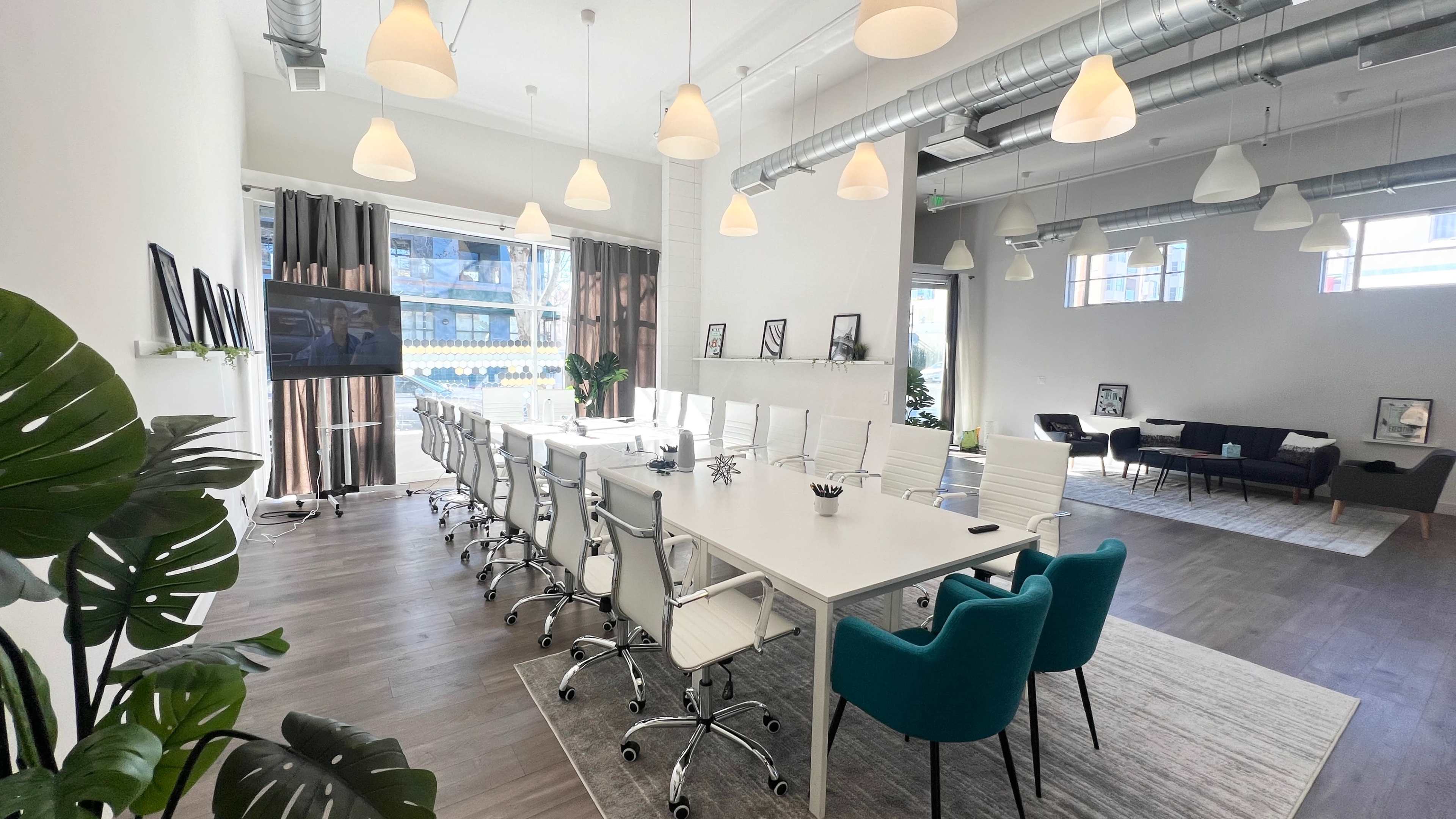A modern conference room features a long white table surrounded by ergonomic chairs, with large windows and decorative plants.