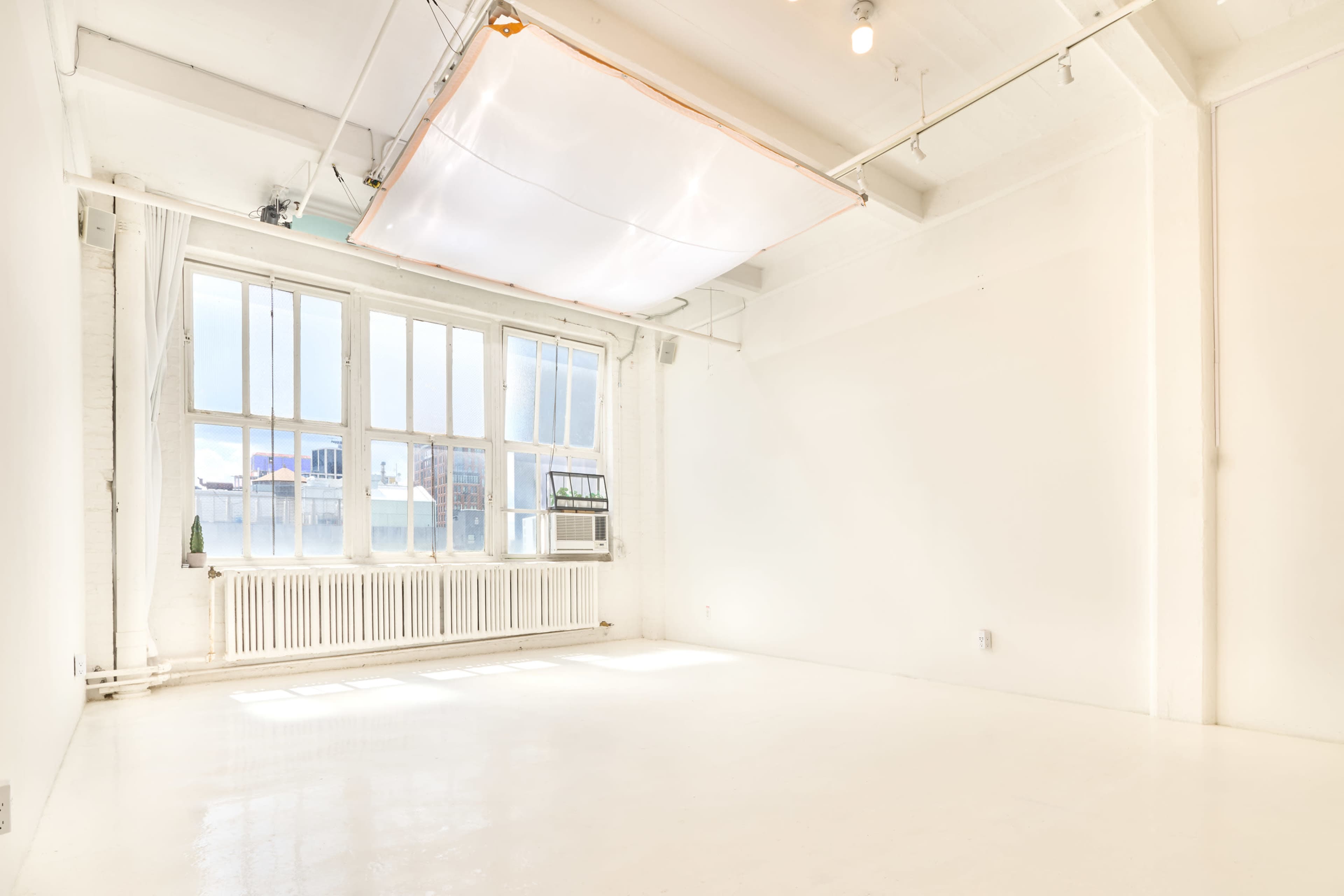 The image shows a bright, empty studio space with large windows and white walls.
