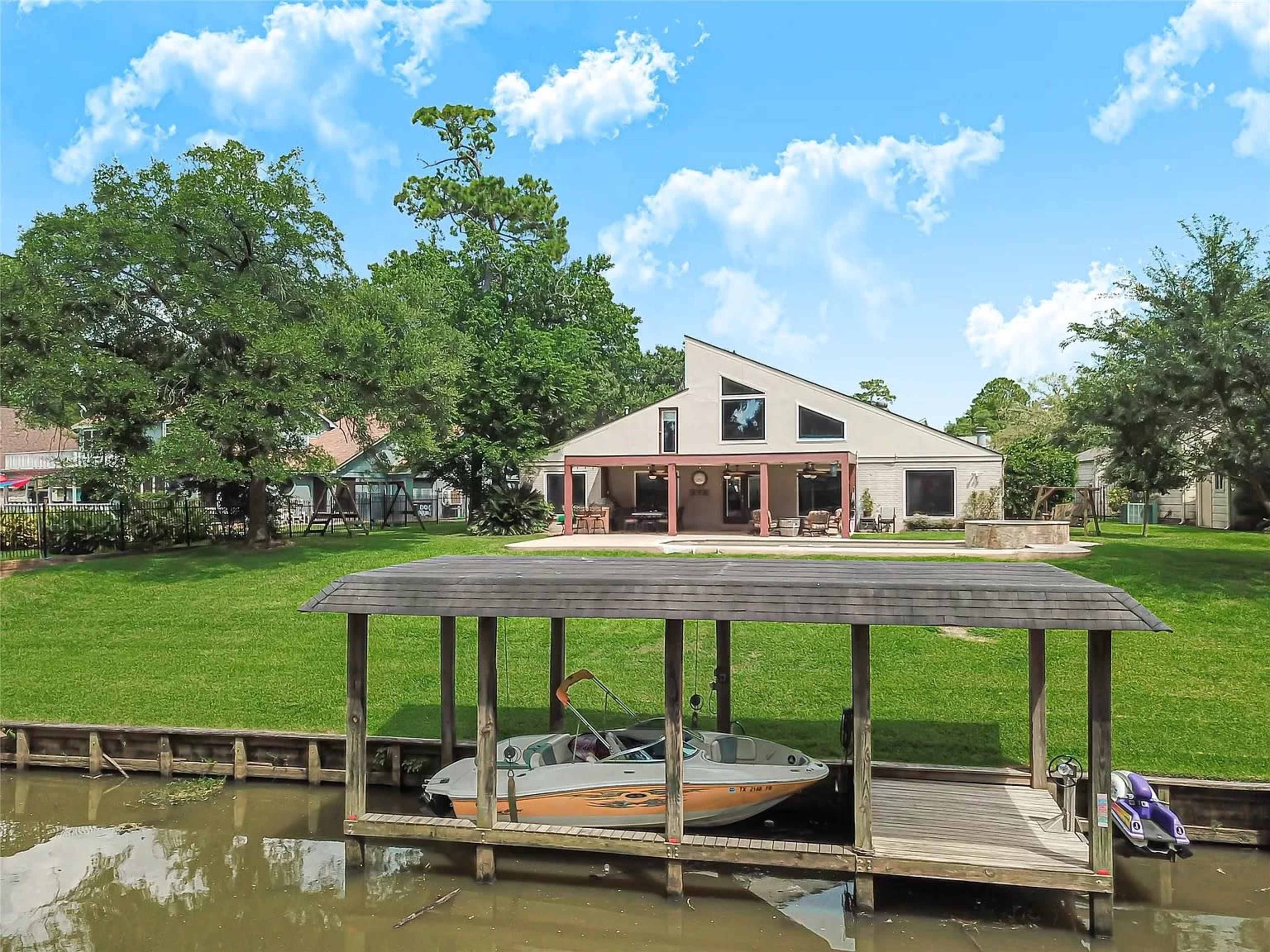 A modern house with large windows overlooks a grassy yard and a boat dock on the water.