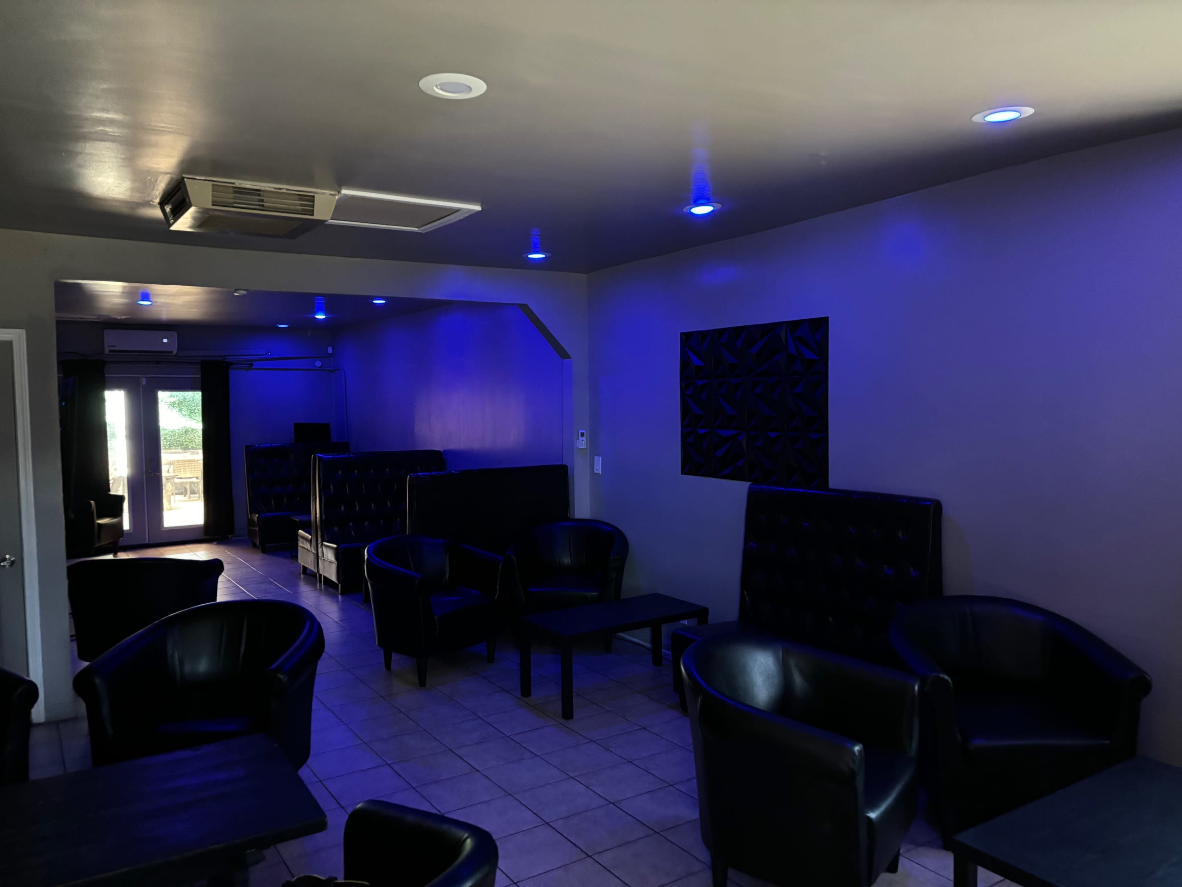 The image shows a dimly lit lounge with black leather seating, tiled flooring, and blue accent lights on the walls and ceiling.