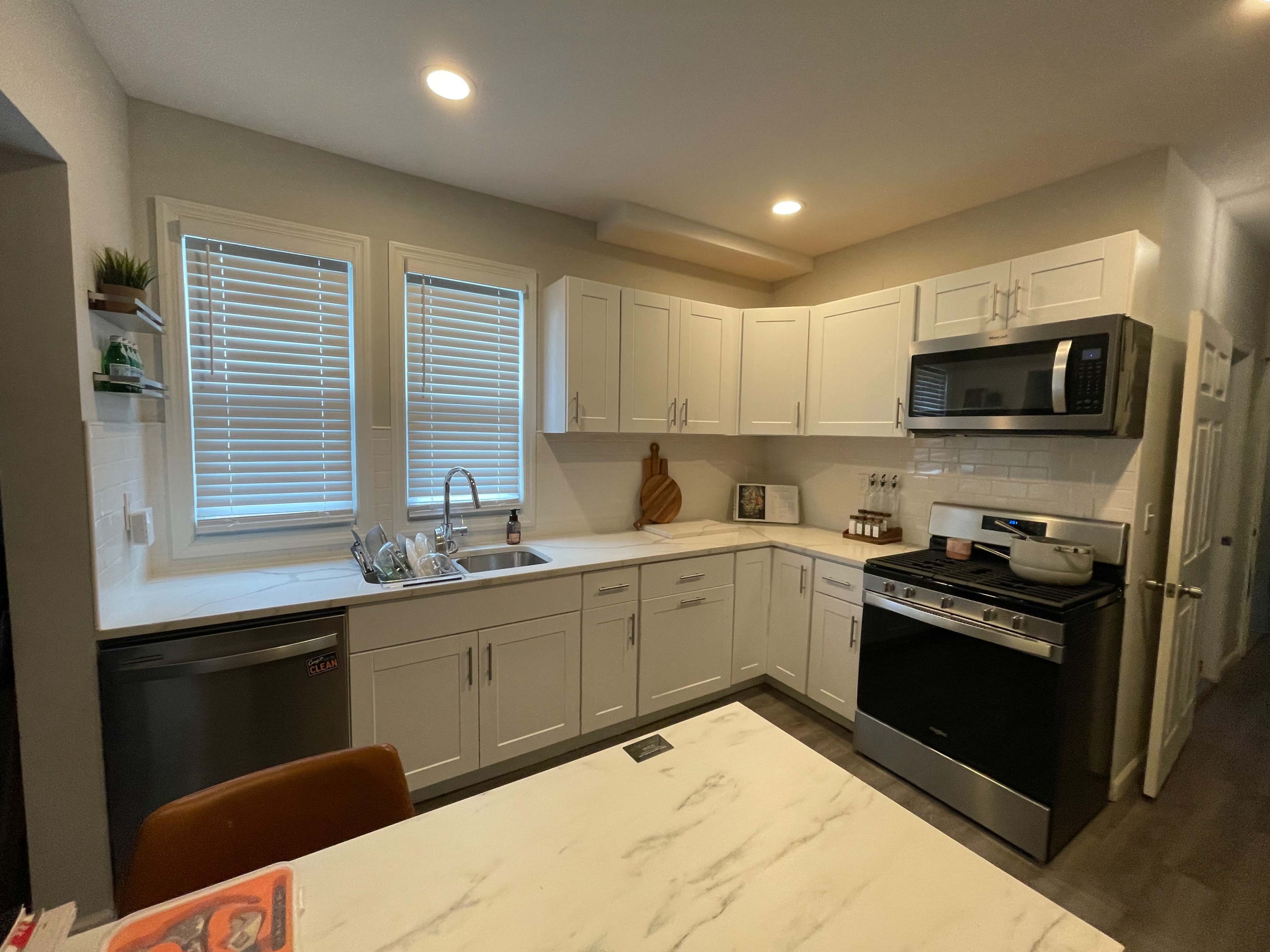 A modern kitchen featuring white cabinets, a stainless steel refrigerator, a black stove, and a dining table with a few items on top.