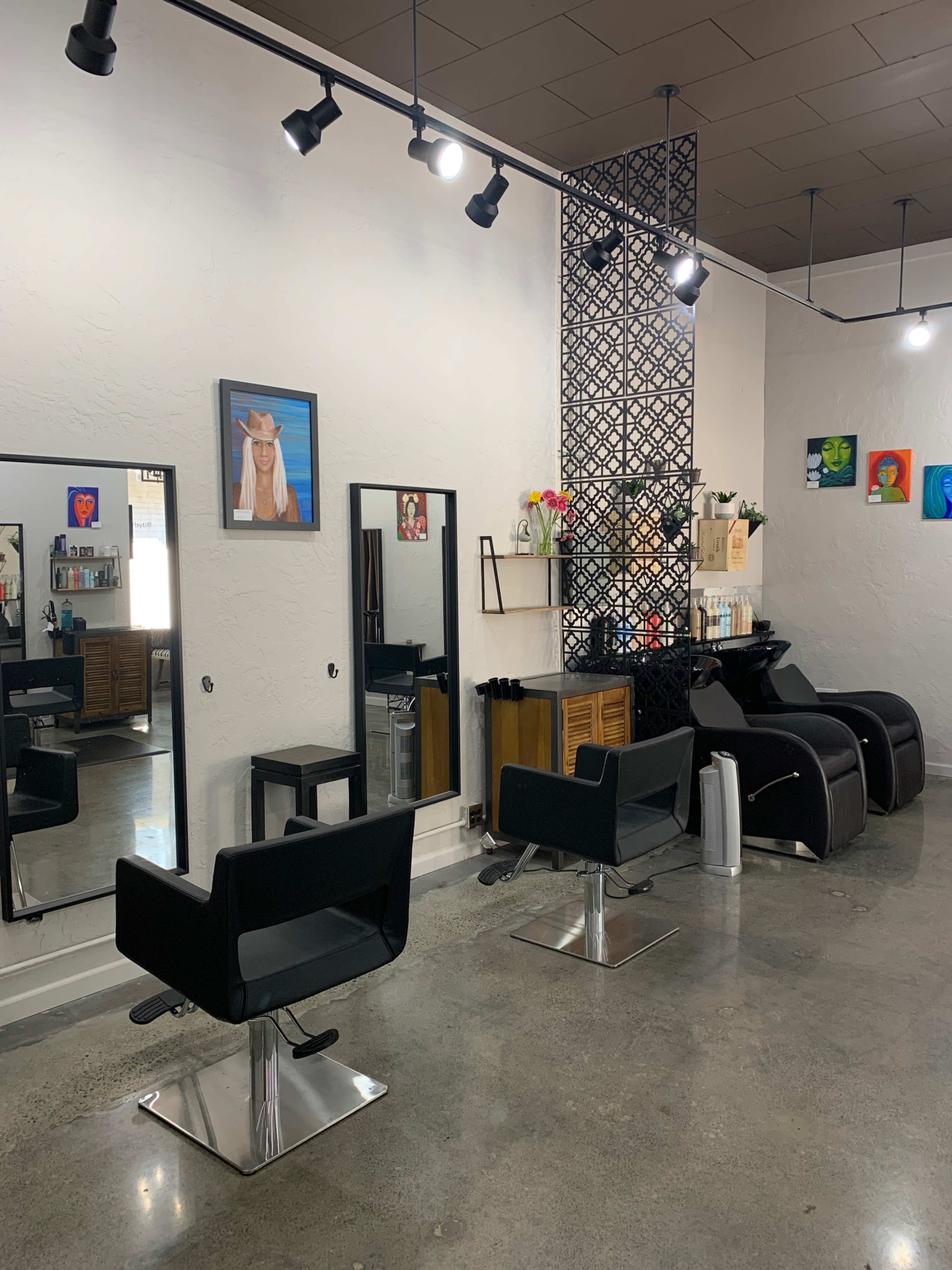 A modern hair salon featuring black styling chairs, two mirrors, and a decorative wall with artwork and hair products.
