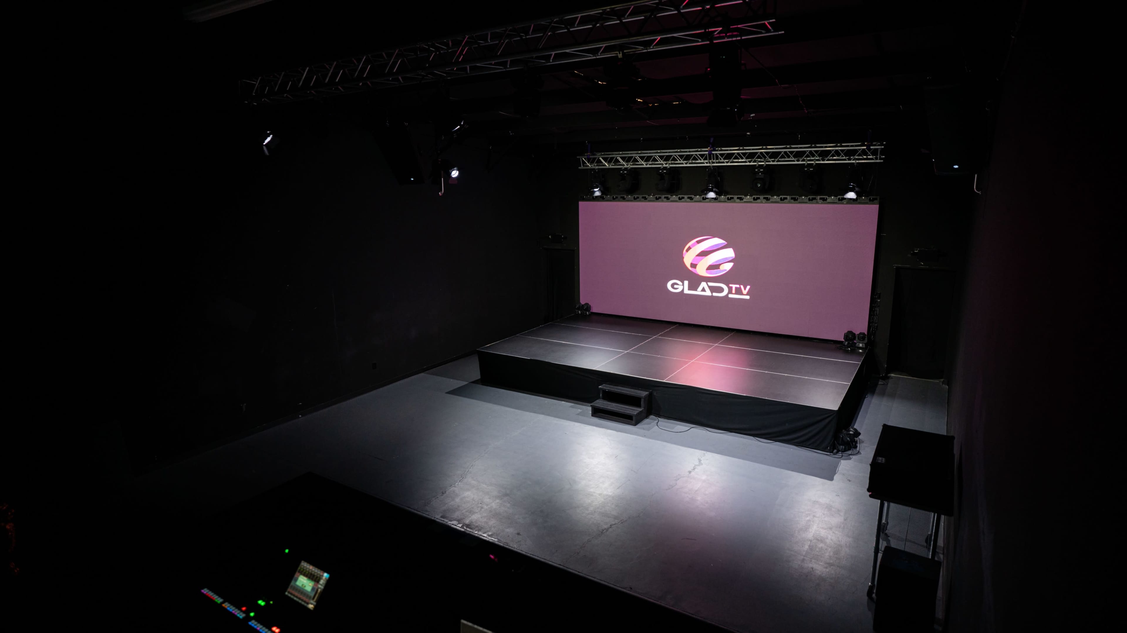 A stage setup with a large screen displaying the logo for GLAD TV in a darkened room.