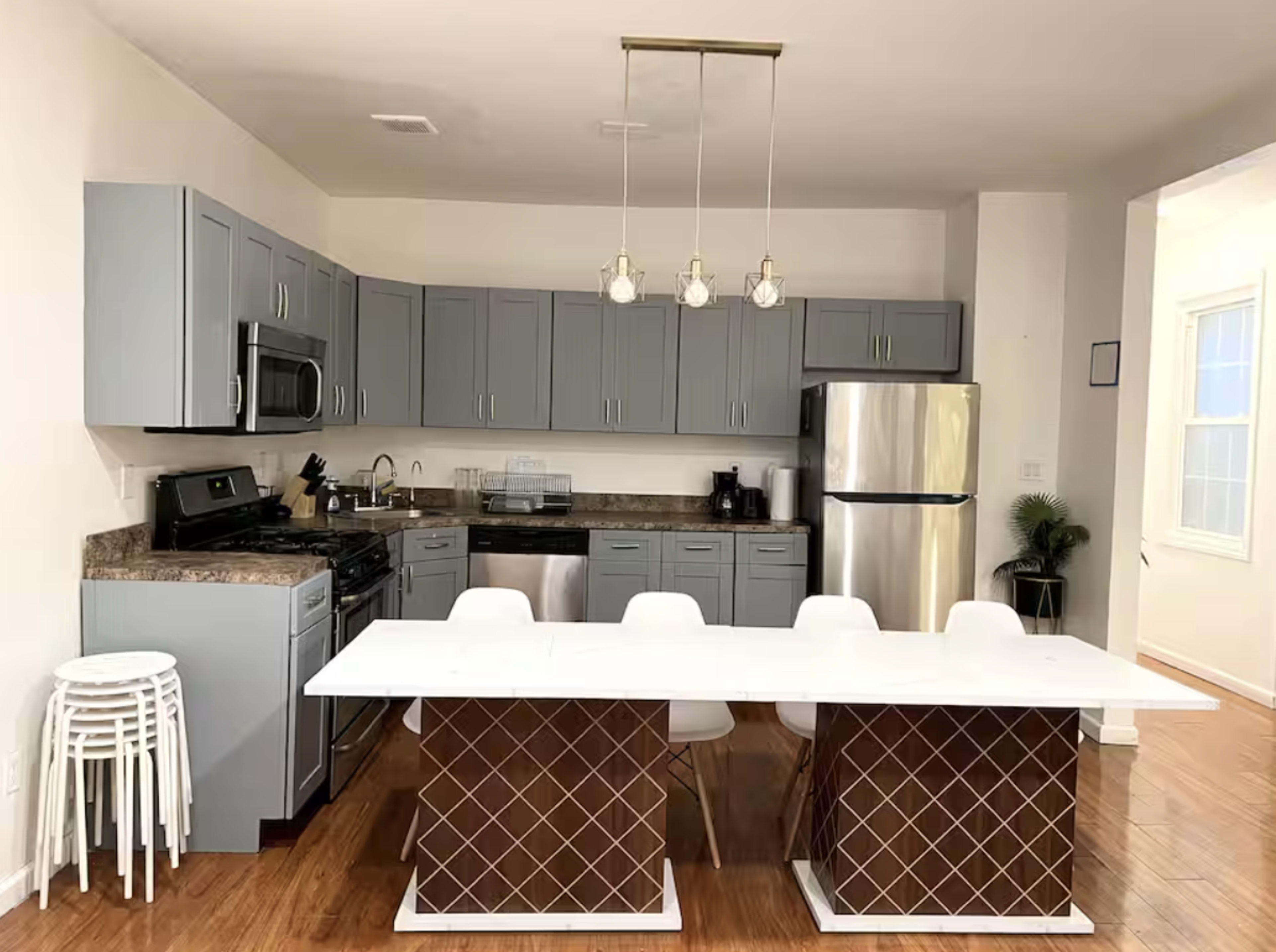 The image shows a modern kitchen with gray cabinets, stainless steel appliances, and a central island with a white countertop and patterned base.