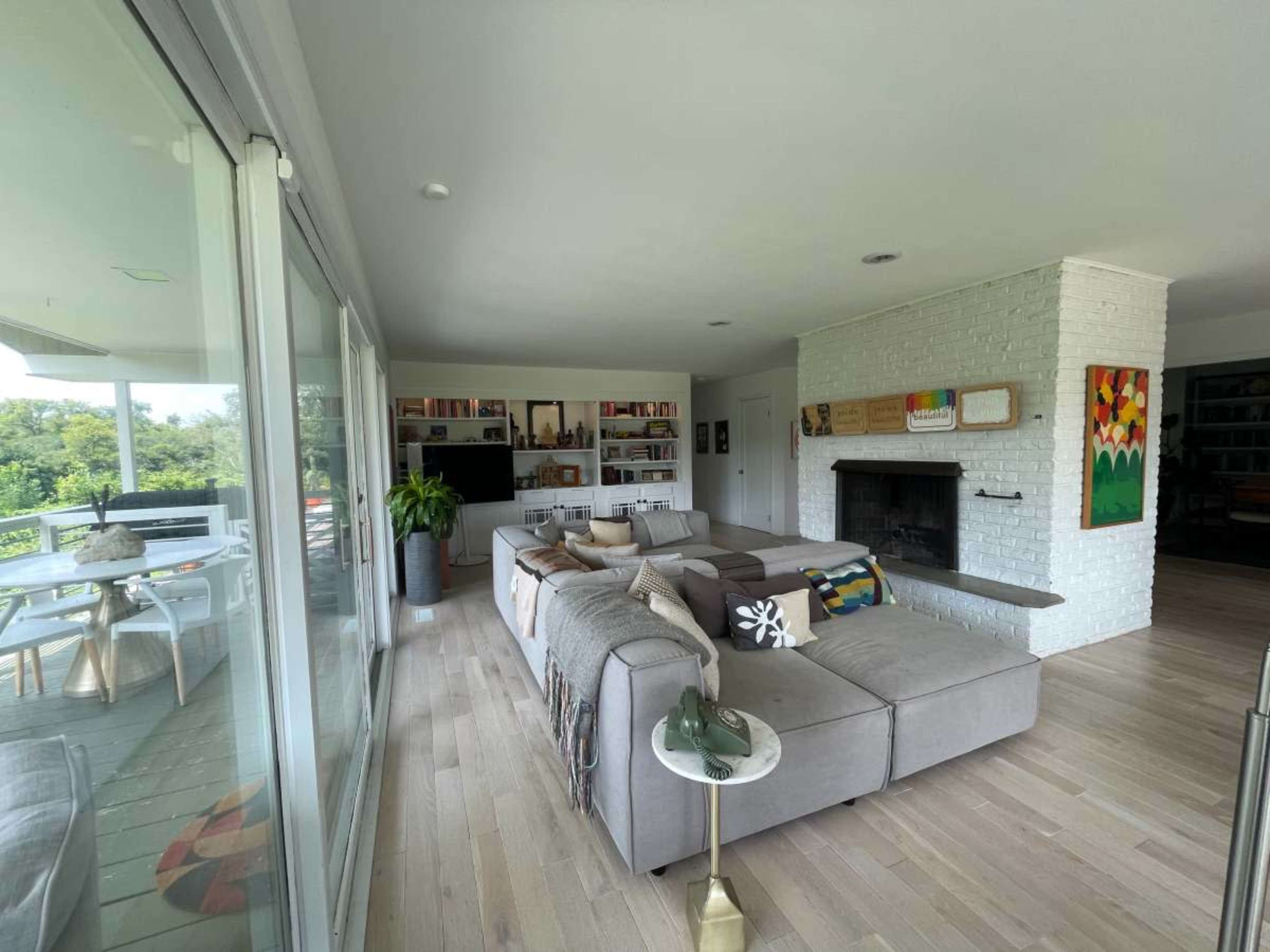 A modern living room with a large sectional sofa, a coffee table, shelves filled with books, and a white brick fireplace.