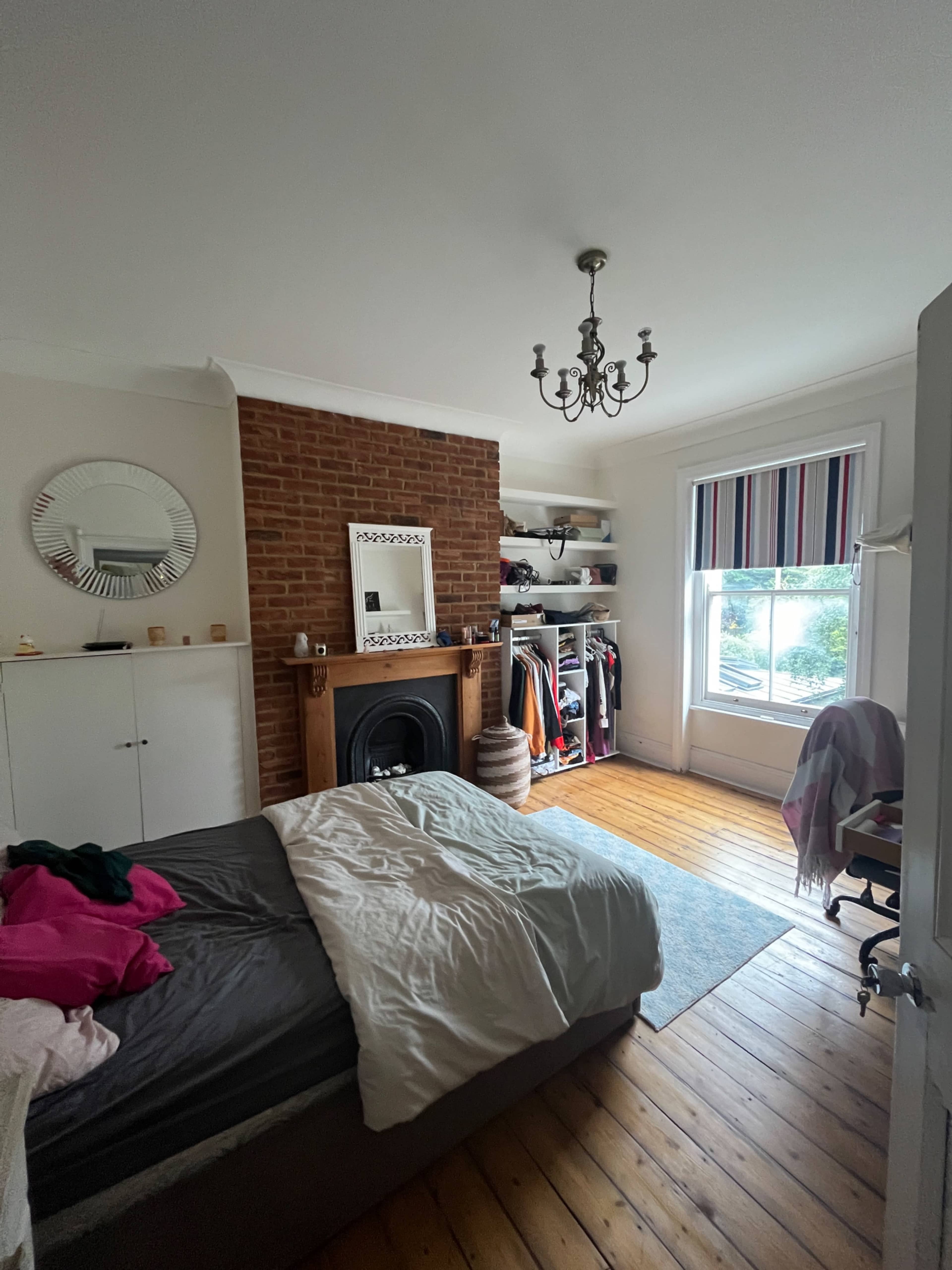 The image shows a bedroom featuring a bed, a fireplace with a mantel, a wardrobe, and a window with striped curtains.