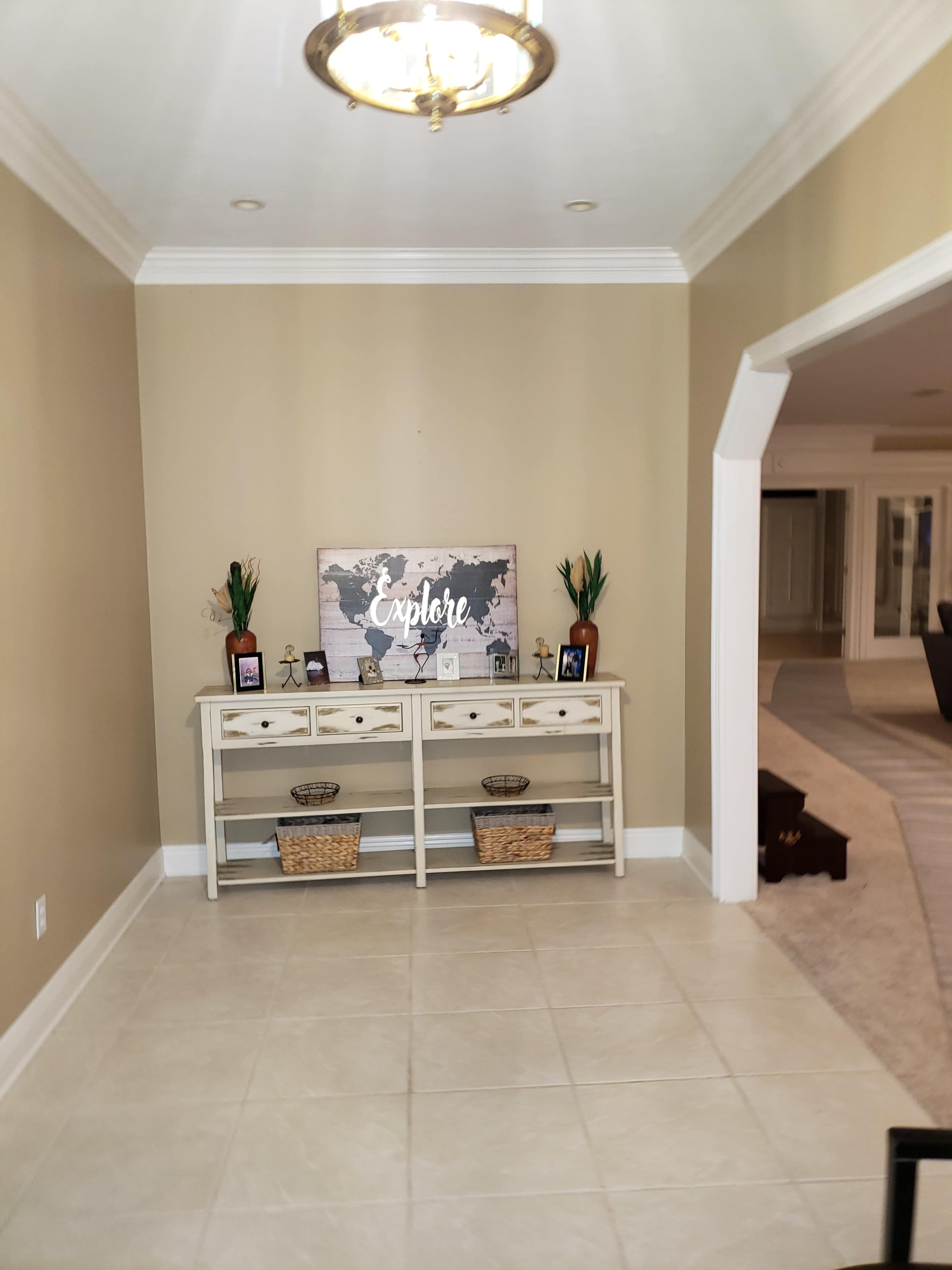 A foyer features a light fixture overhead, a white console table with decorative items, and a map artwork on the wall.