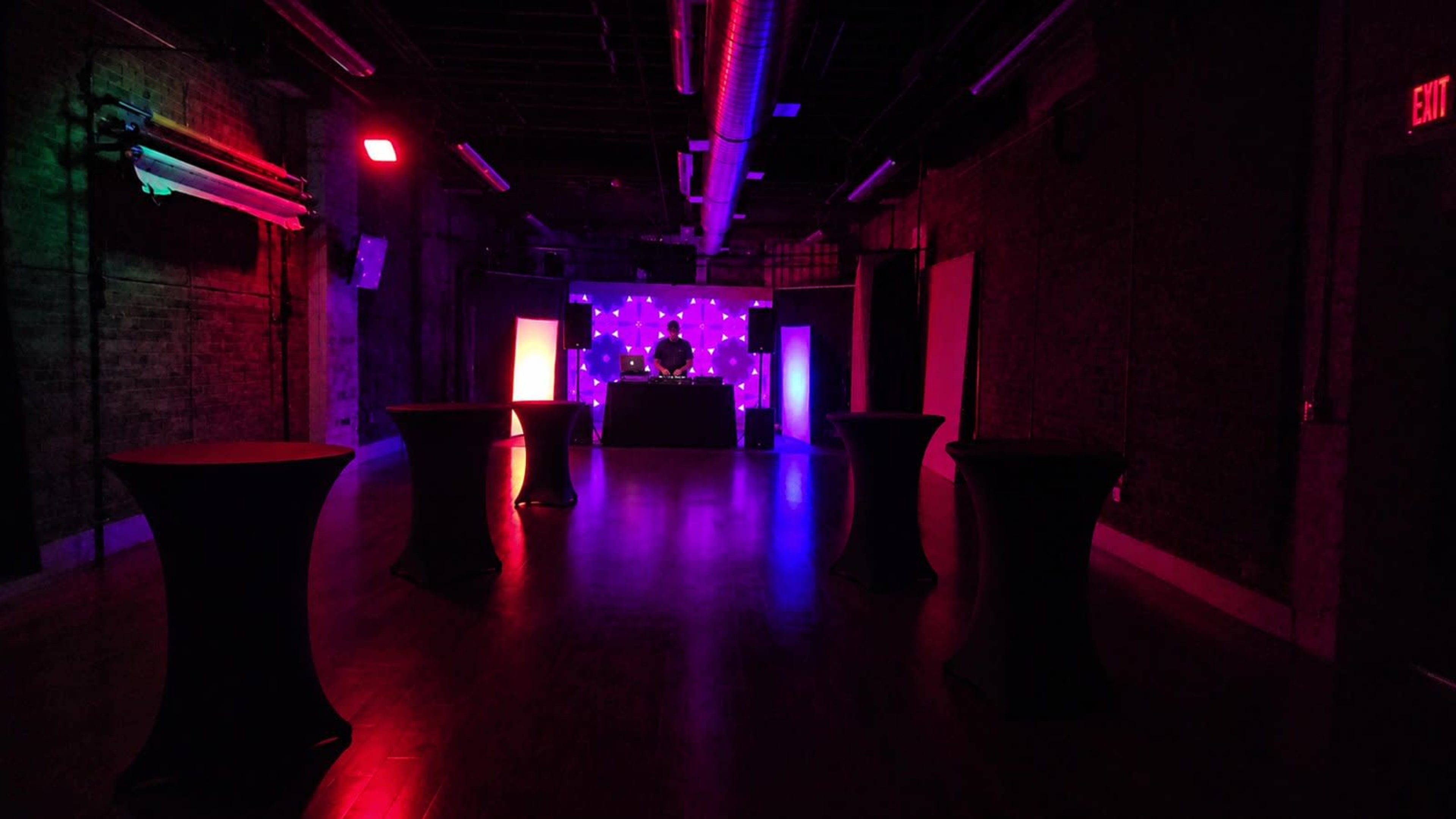 The venue features a dimly lit space with illuminated tables and a backdrop displaying colorful lights, suggesting a setup for an event or party.