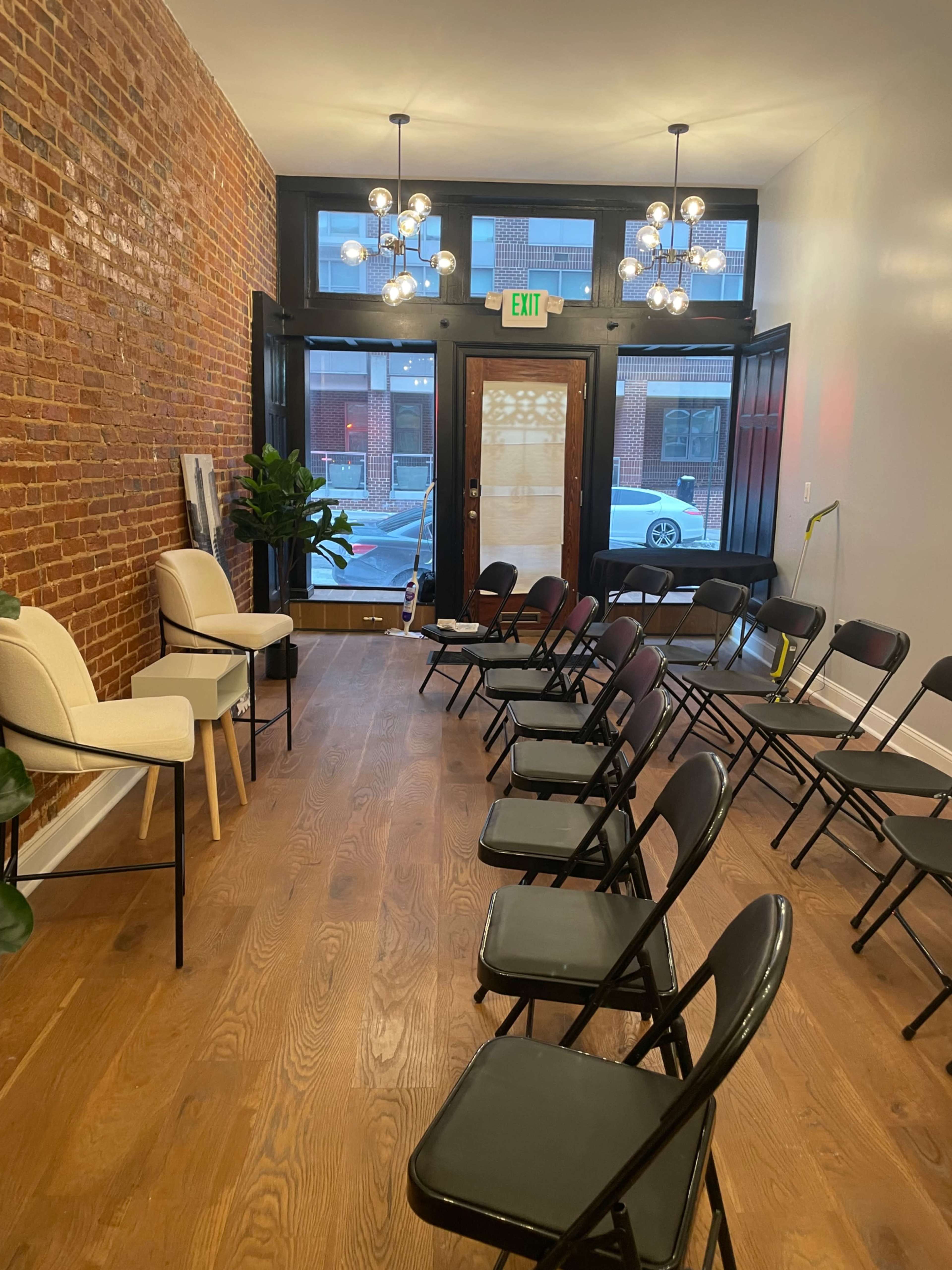 A room with wooden flooring, lined with chairs arranged in two rows, and featuring a large window with natural light illuminating the space.