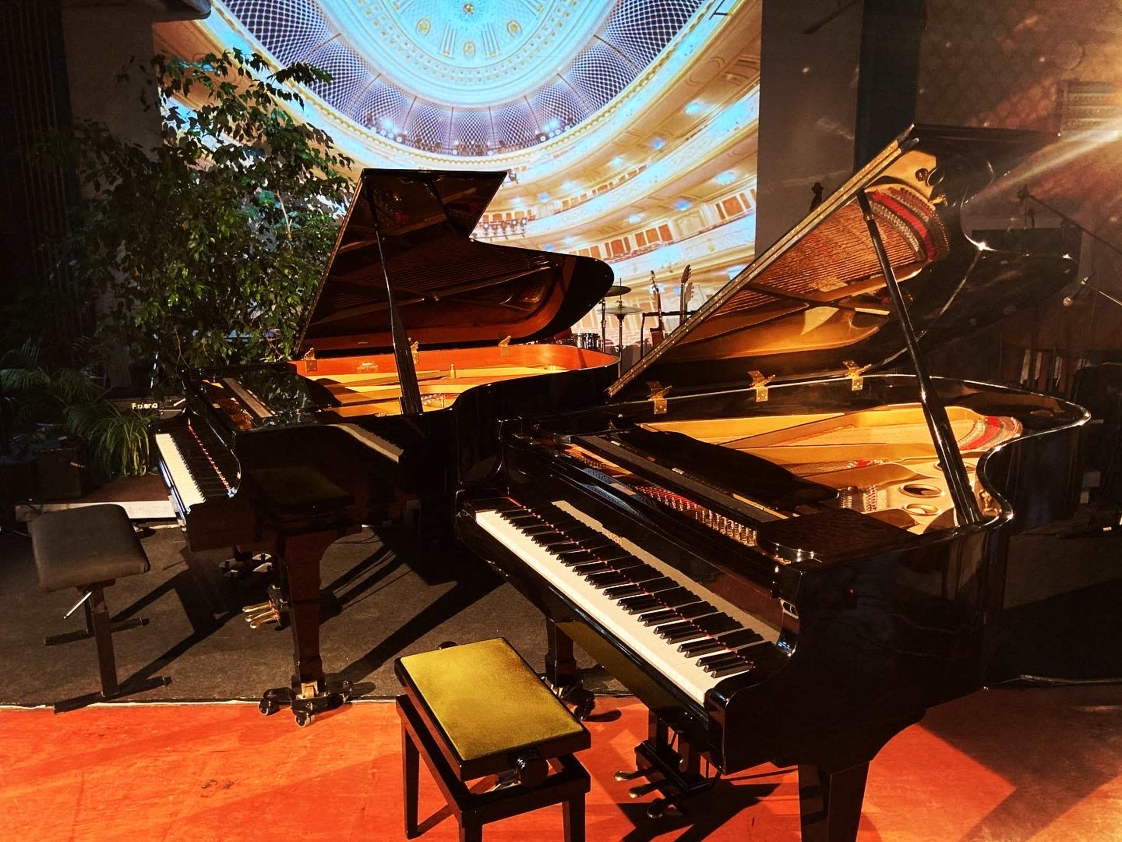 Two grand pianos are positioned side by side on a stage with a decorative backdrop.