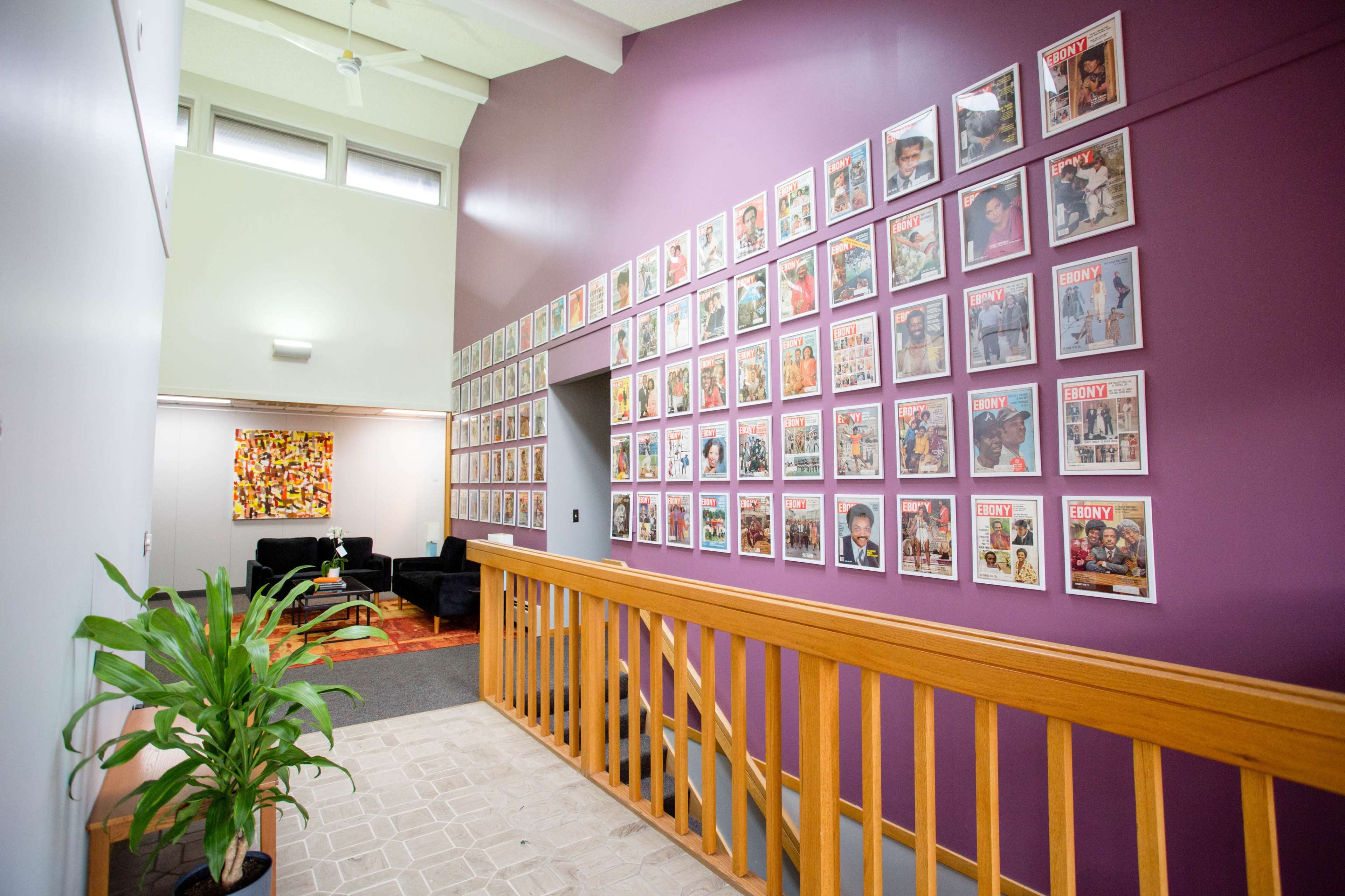 A hallway featuring walls adorned with framed magazine covers, alongside a wooden railing and a seating area with a black couch in the background.