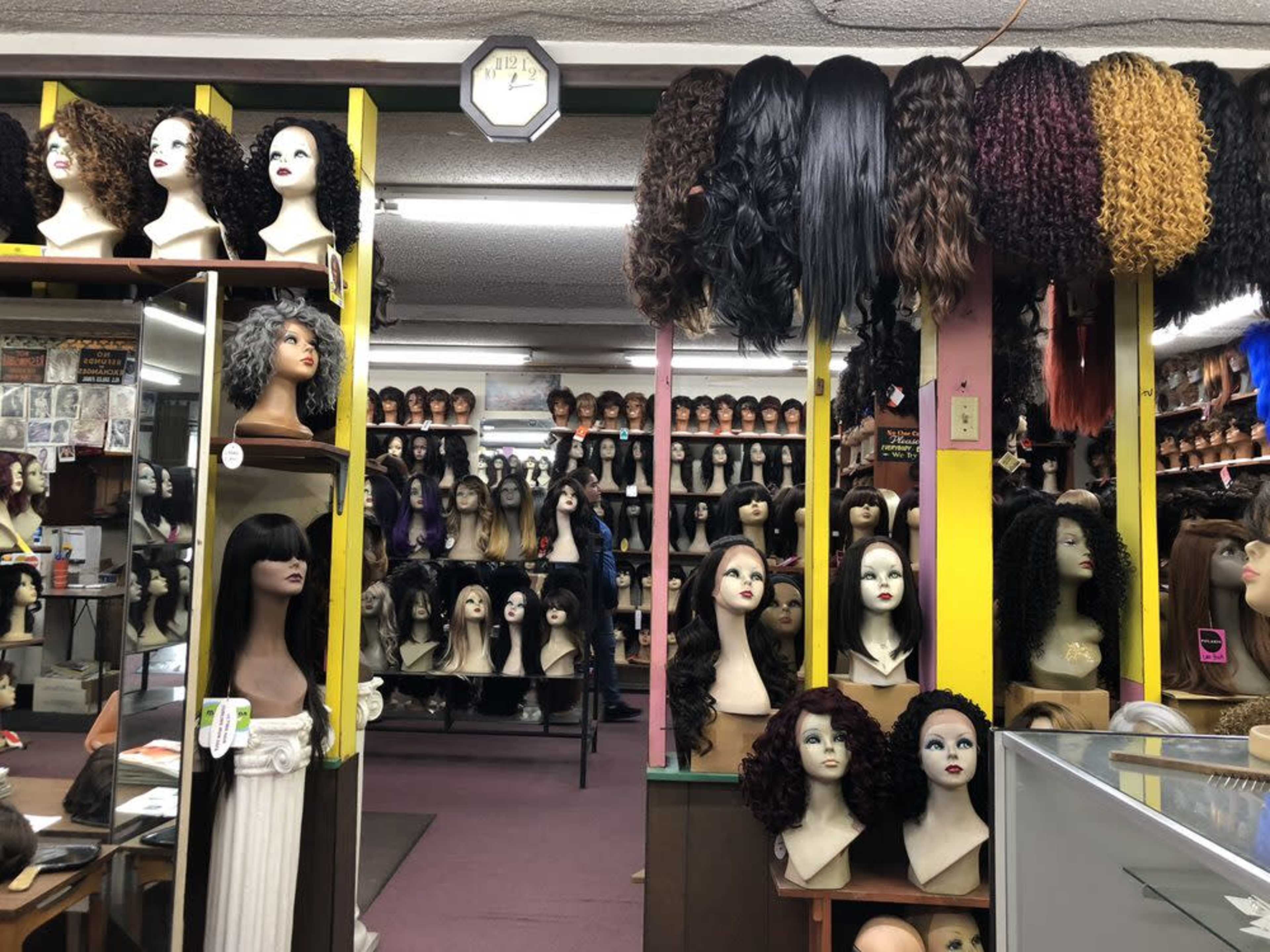 A wig shop filled with mannequins wearing various styled wigs, with rows of additional wigs displayed on shelves behind them.