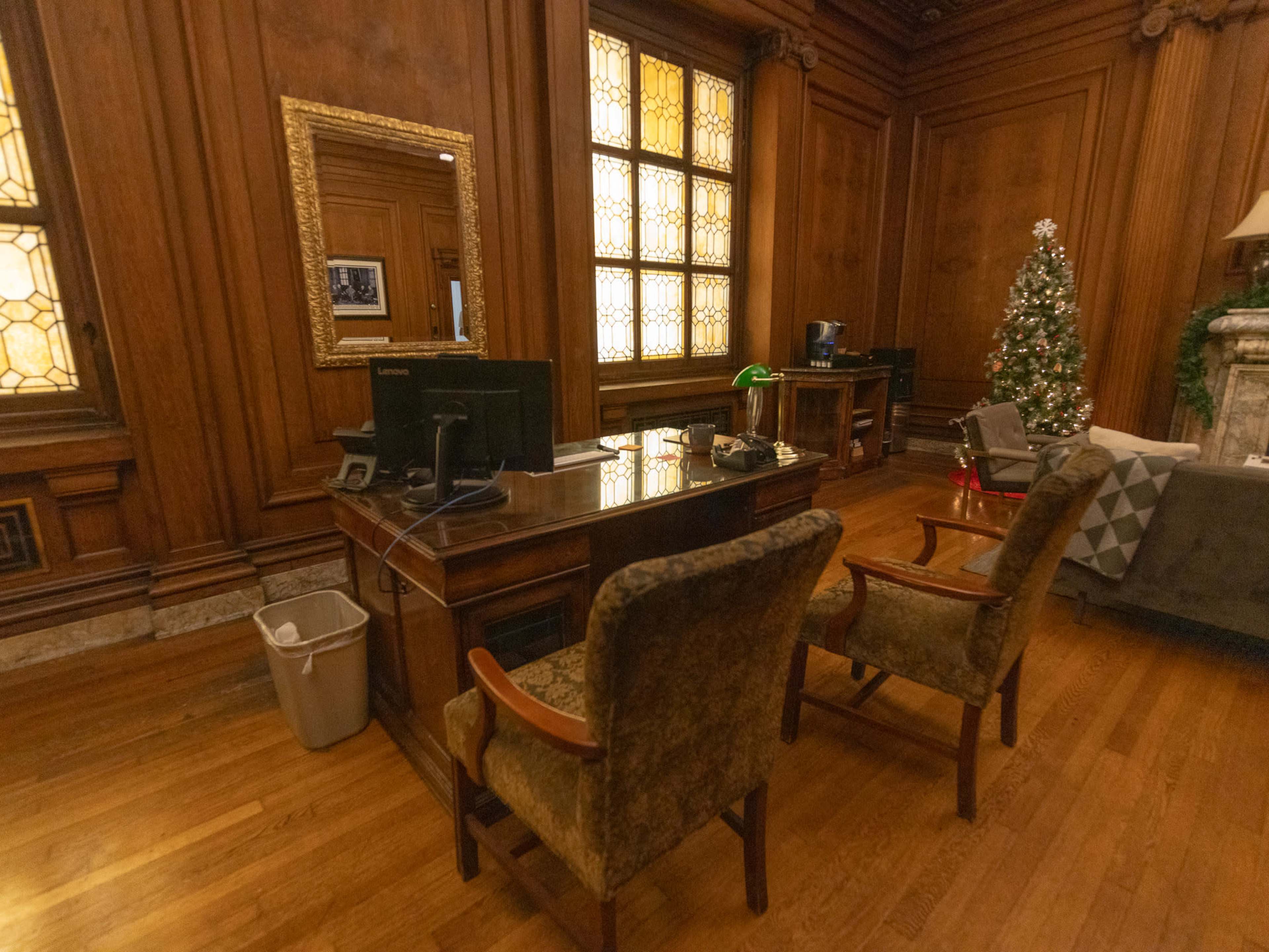 The image shows a wooden office space with two chairs facing a desk, a computer on the desk, and a decorative Christmas tree in the corner.