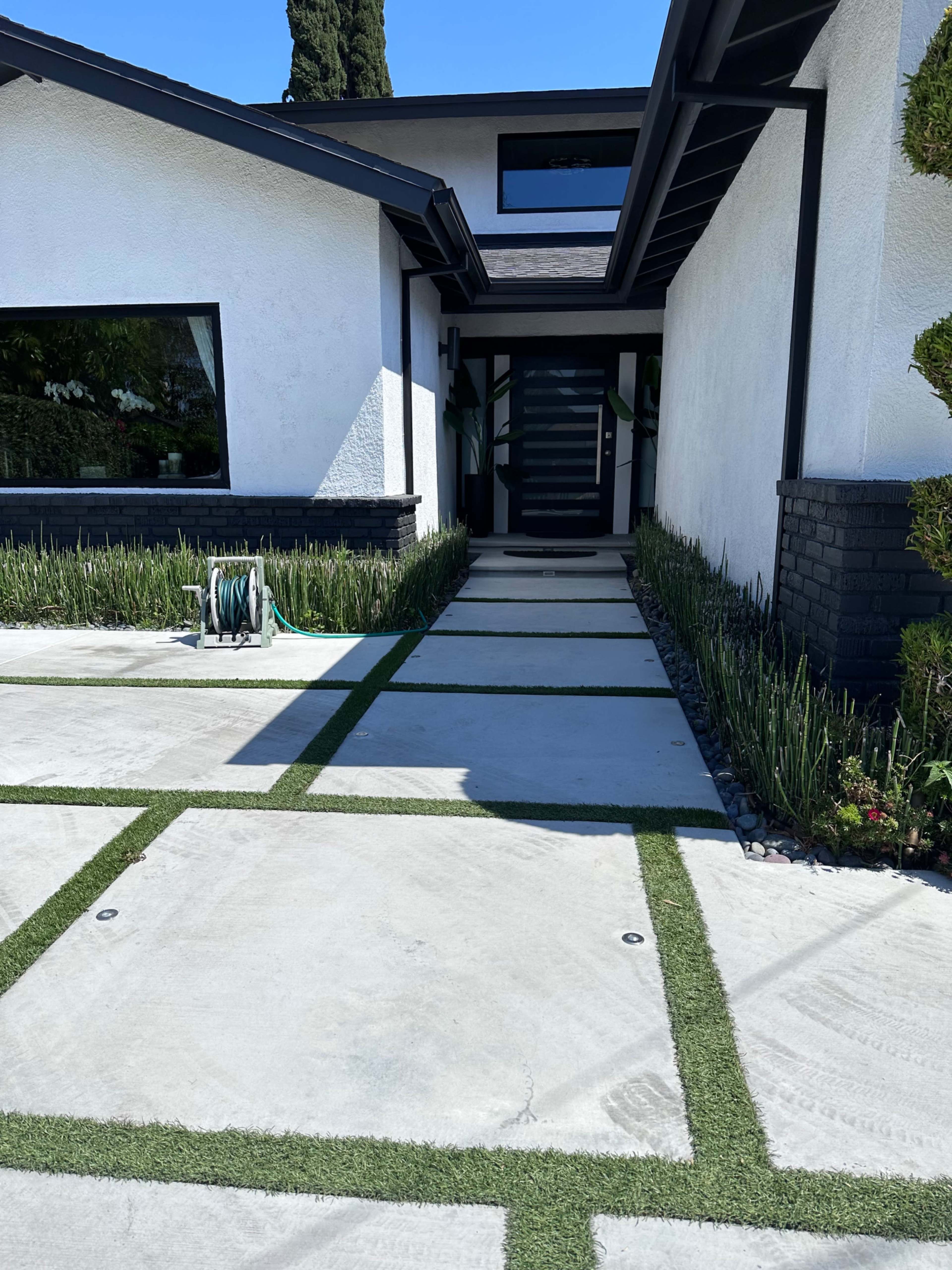 A modern home entrance with a concrete pathway bordered by artificial grass and landscaping.