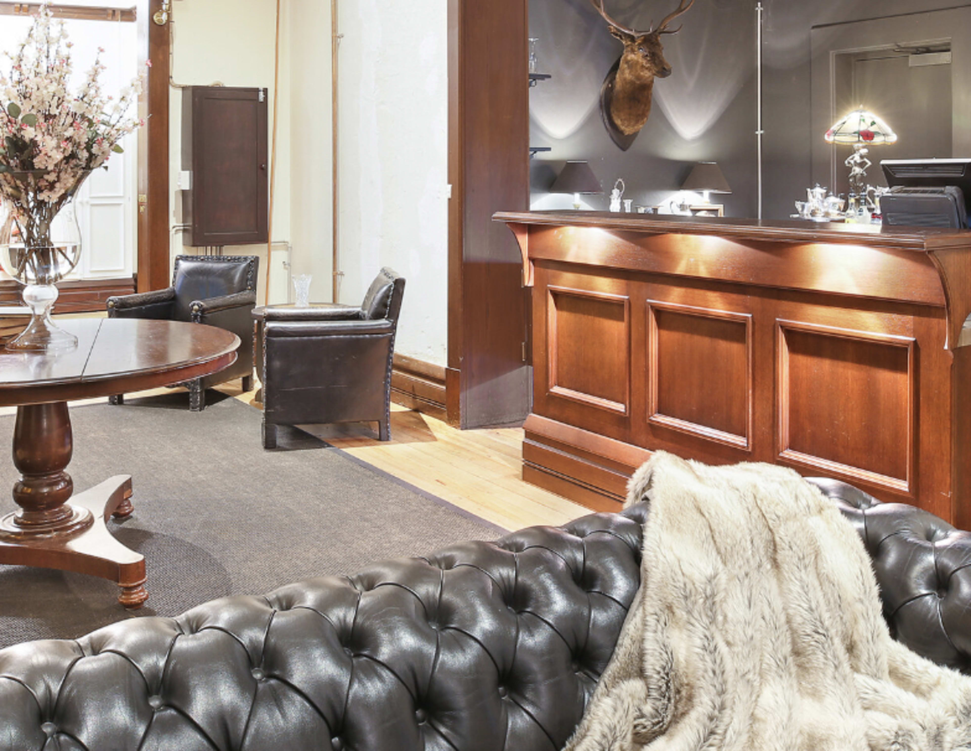 A reception area featuring a wooden front desk, a round dining table, leather chairs, and a decorative taxidermy deer head on the wall.