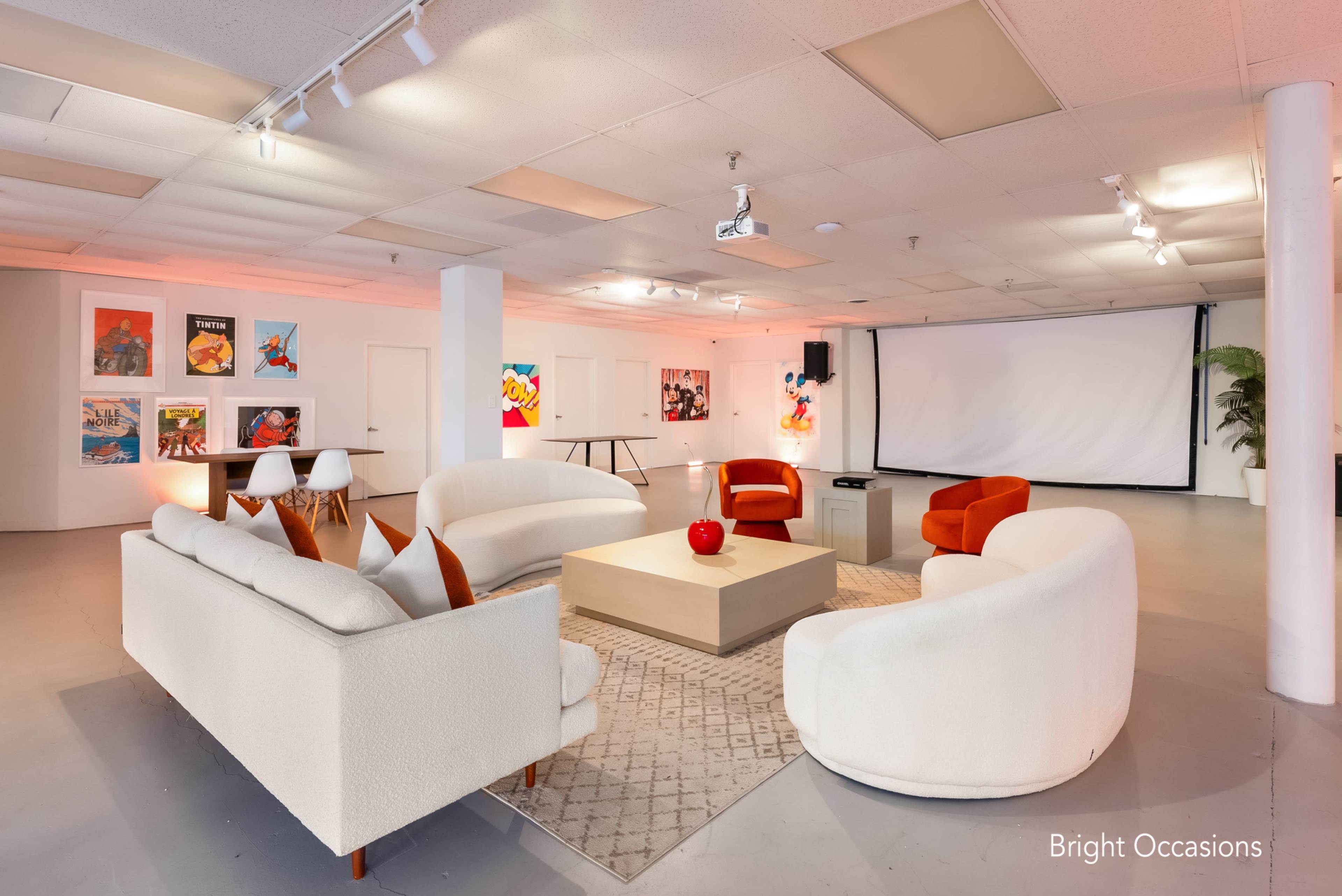The image features a spacious lounge area with soft seating, a coffee table, and colorful artwork on the walls, illuminated by soft lighting.