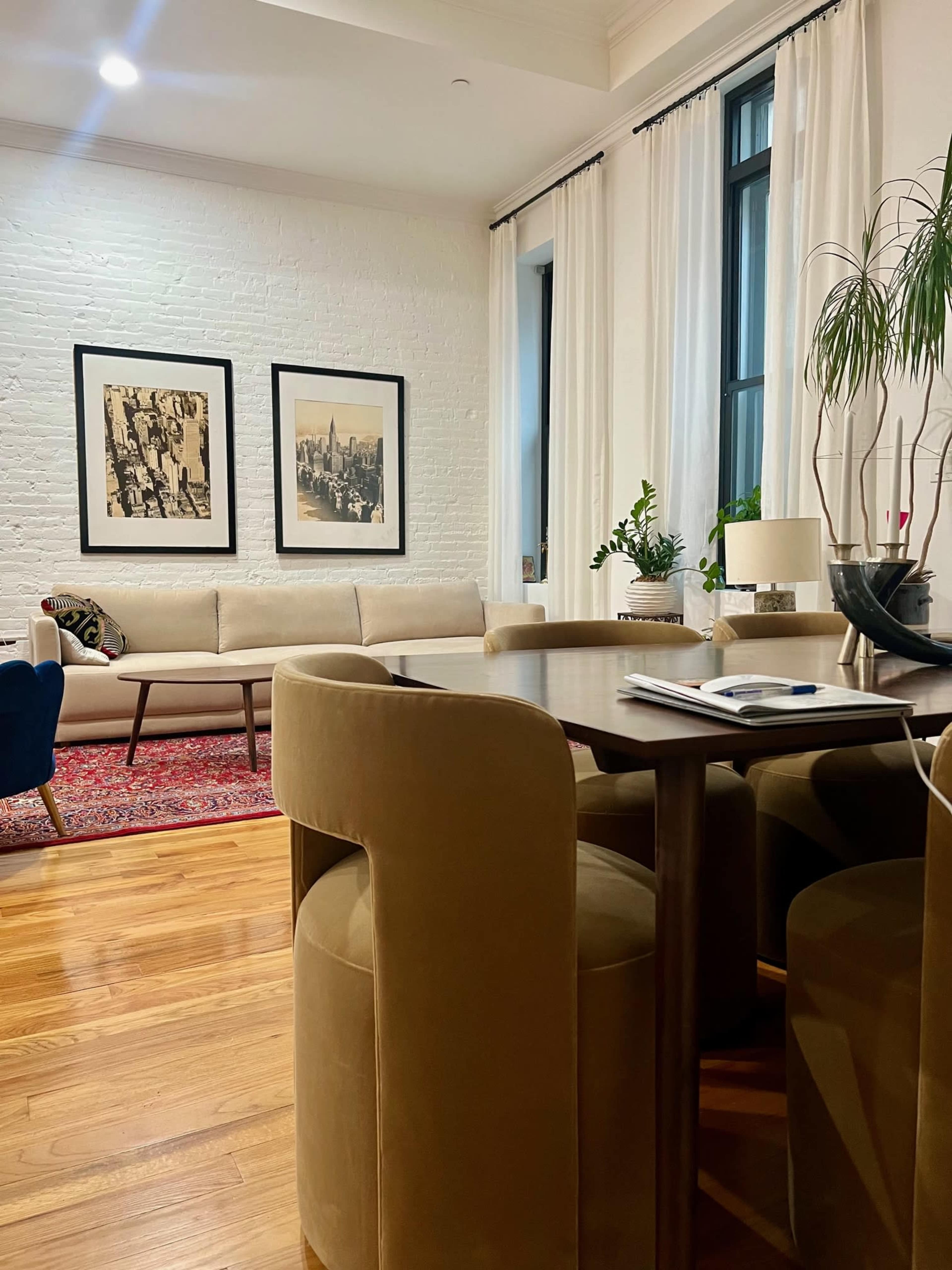 A stylish living space featuring a light-colored couch, two framed pictures on the wall, and a dining table surrounded by upholstered chairs.