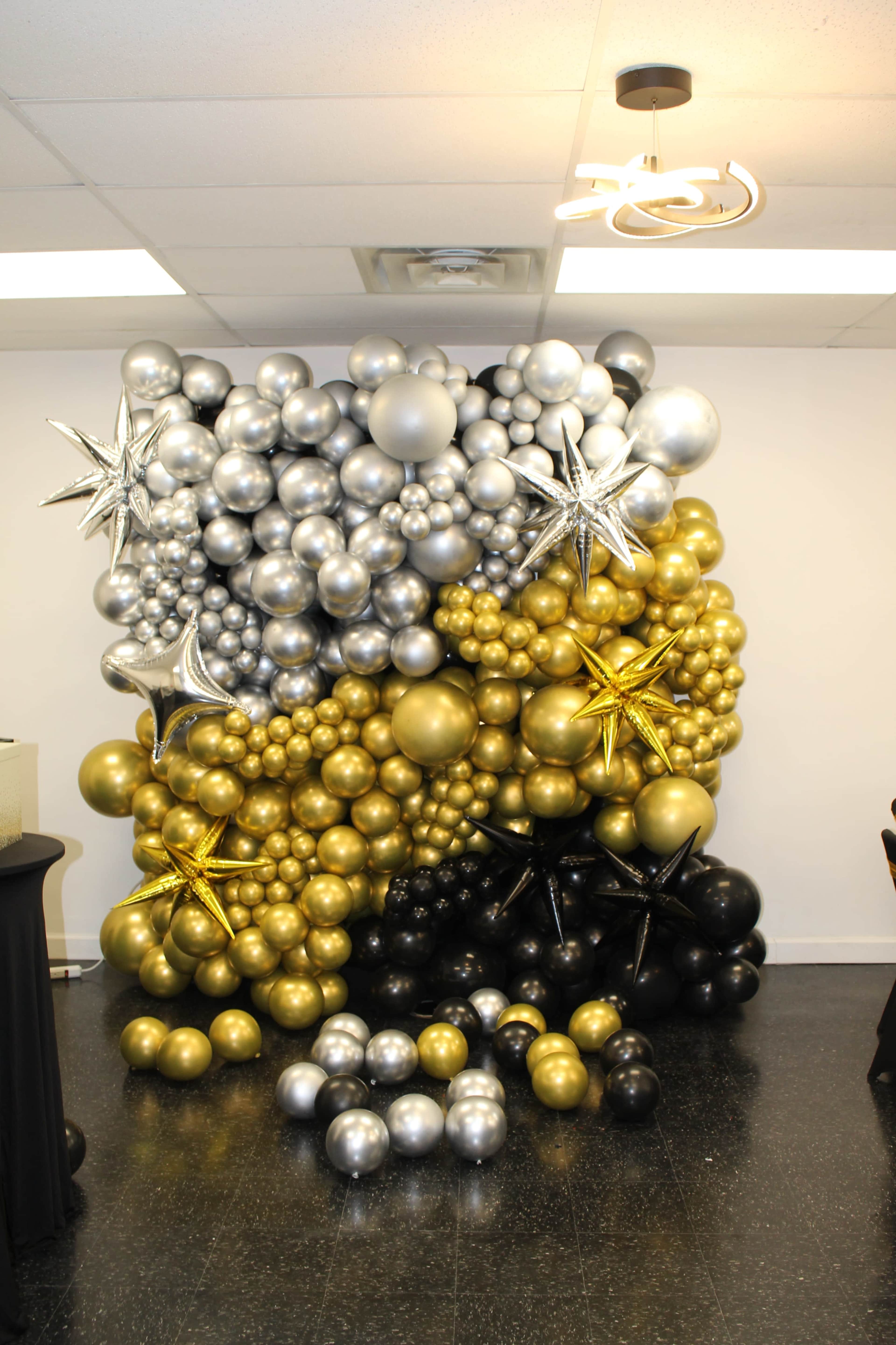 A large decorative balloon wall made of silver, gold, black, and metallic balloons, accented with star-shaped decorations.