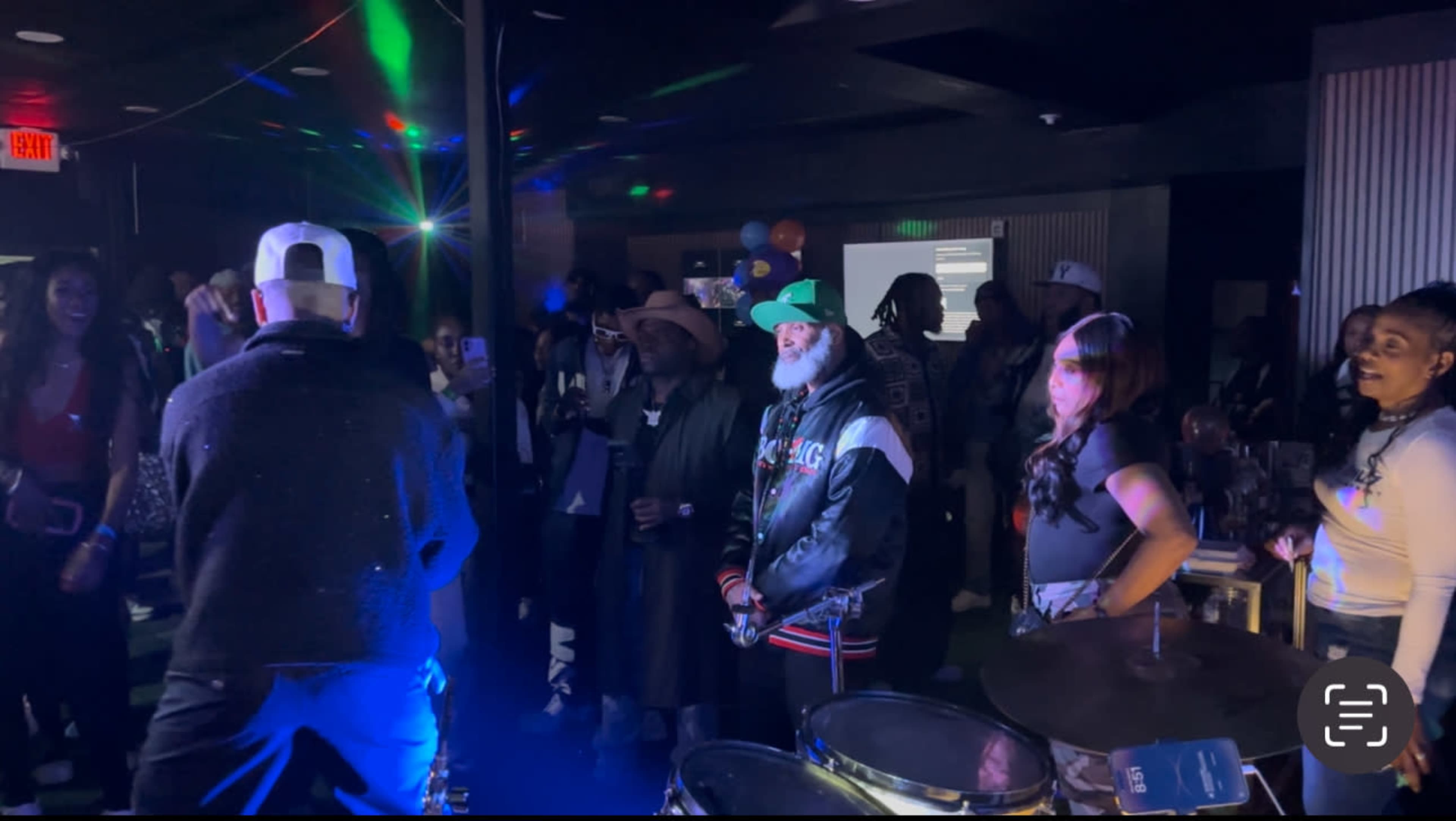 A crowd of people enjoys a live performance in a dimly lit venue with colorful lights and decorations.