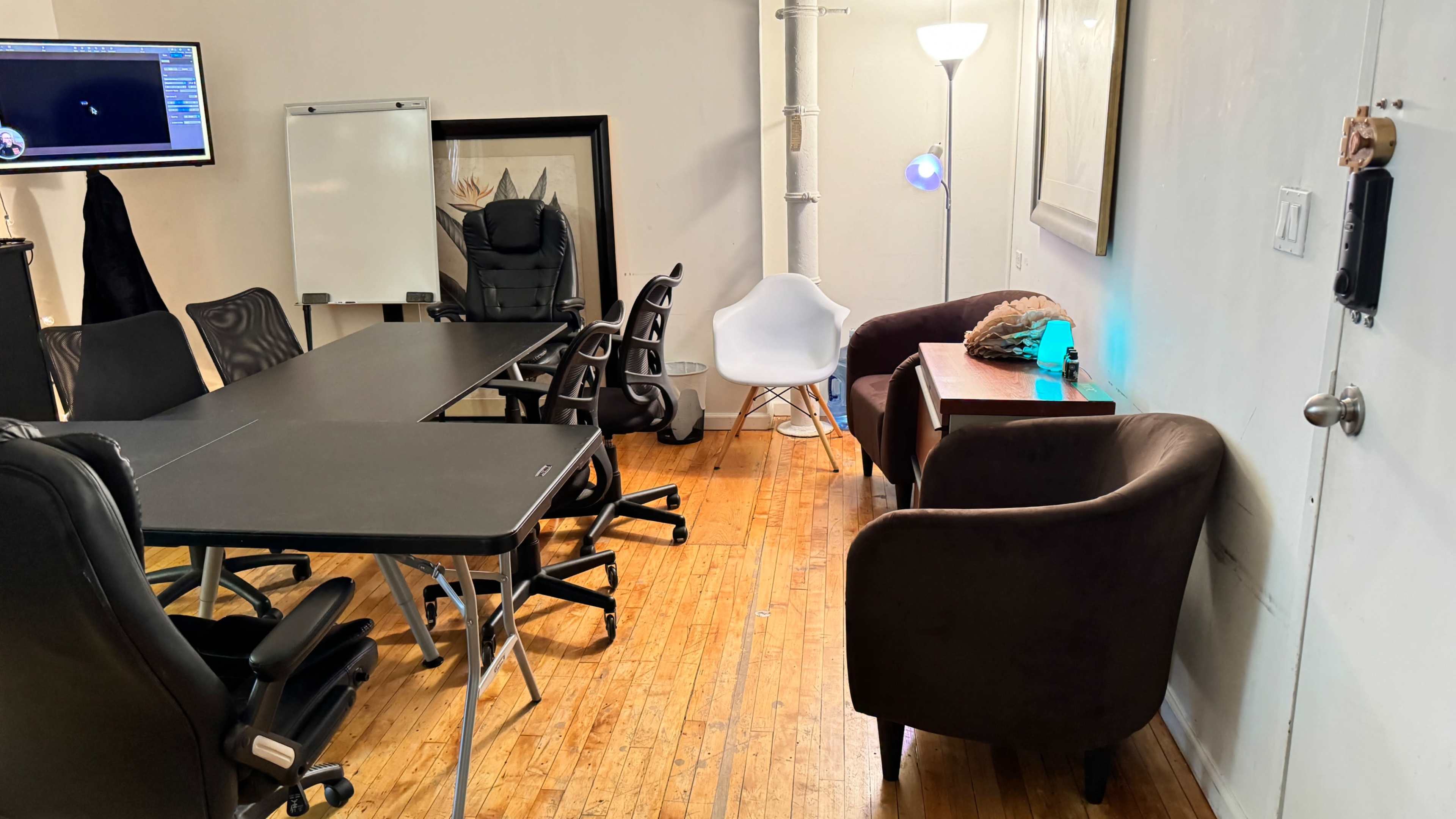A conference room features a long table surrounded by black ergonomic chairs, a whiteboard, and a cozy seating area with two armchairs and a side table.