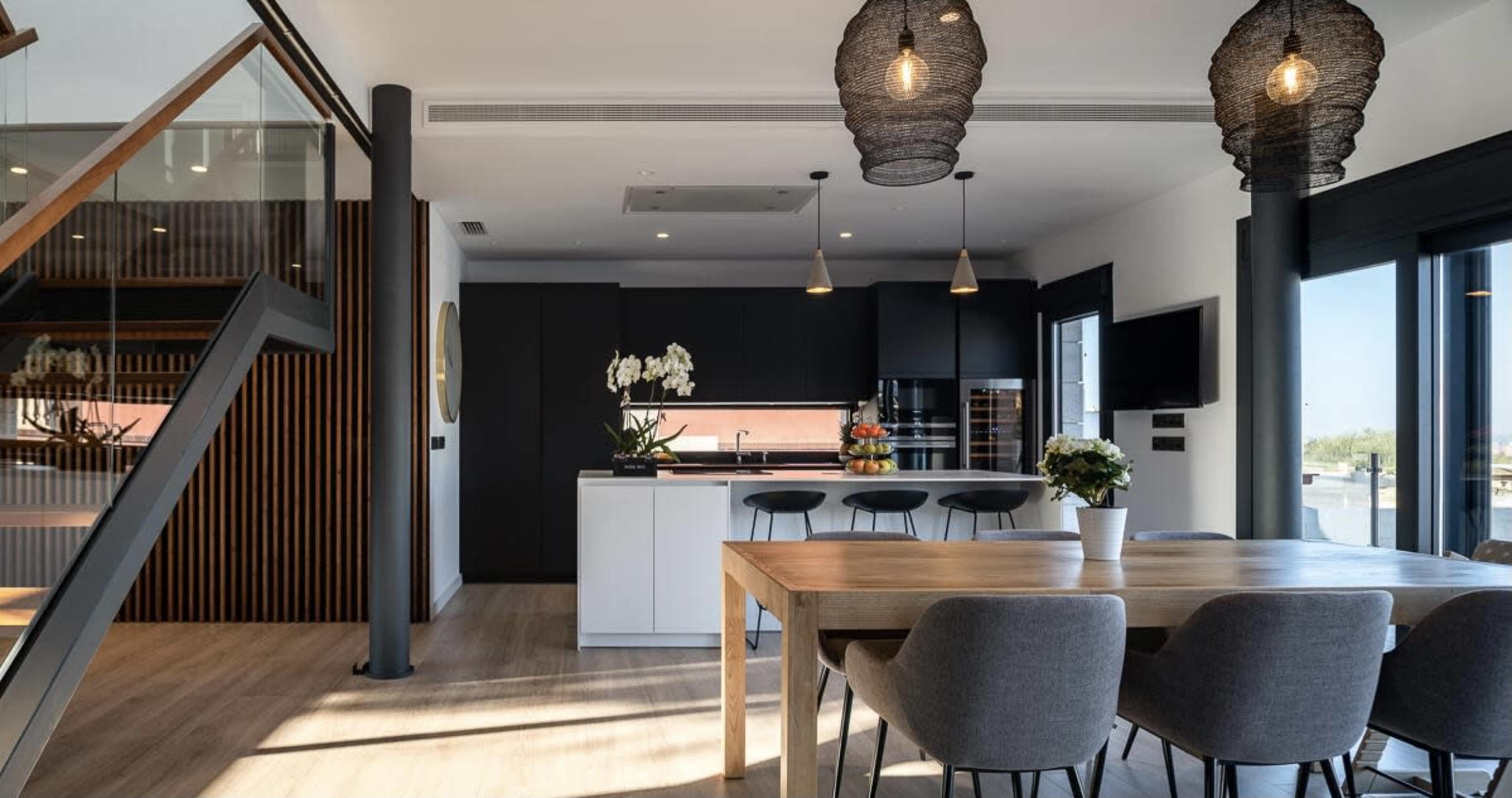The image shows a modern, open-concept kitchen and dining area with a wooden dining table and minimalist decor.