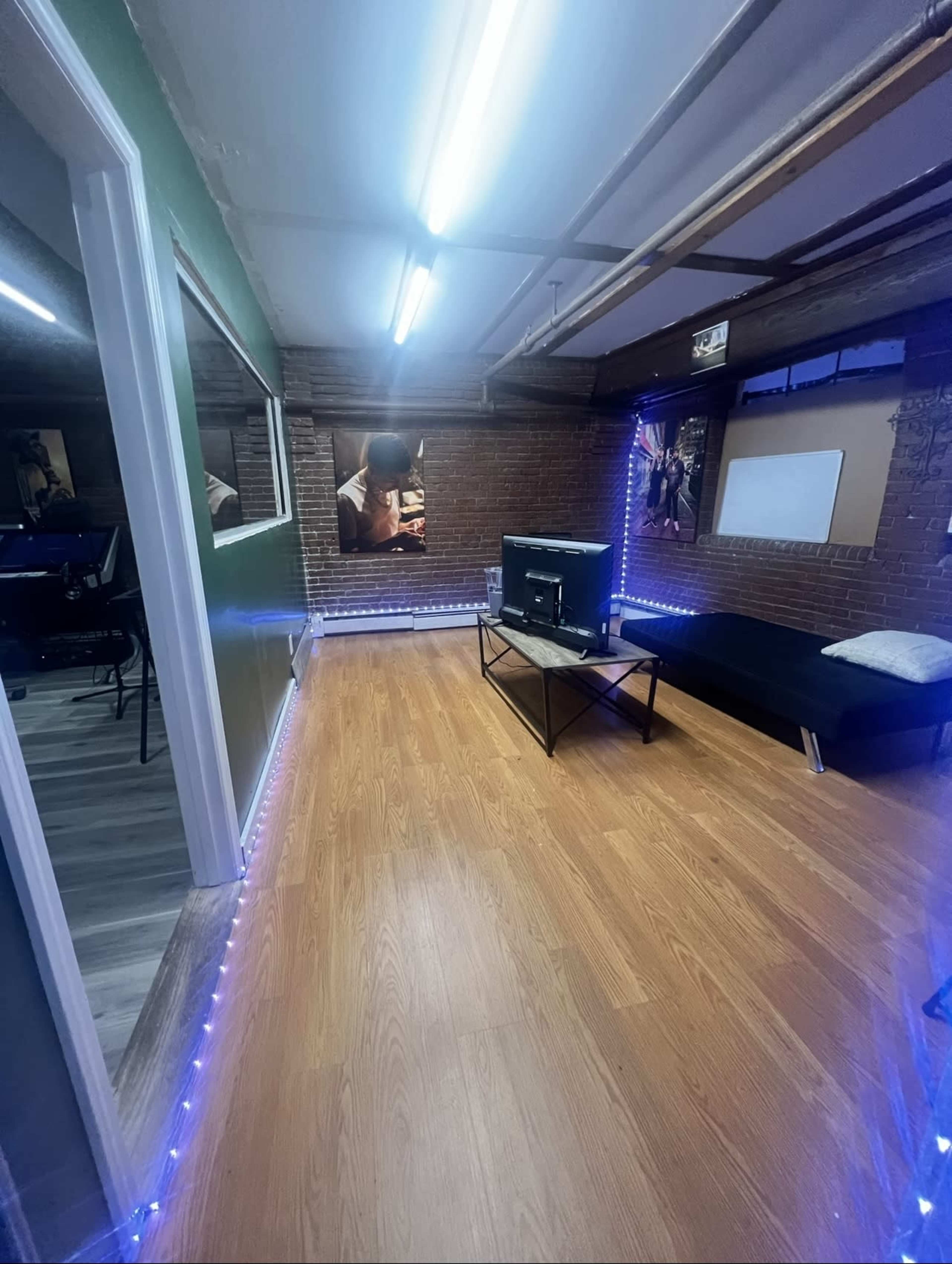 A room with wooden flooring, a black sofa, a coffee table, and LED strip lighting along the walls.