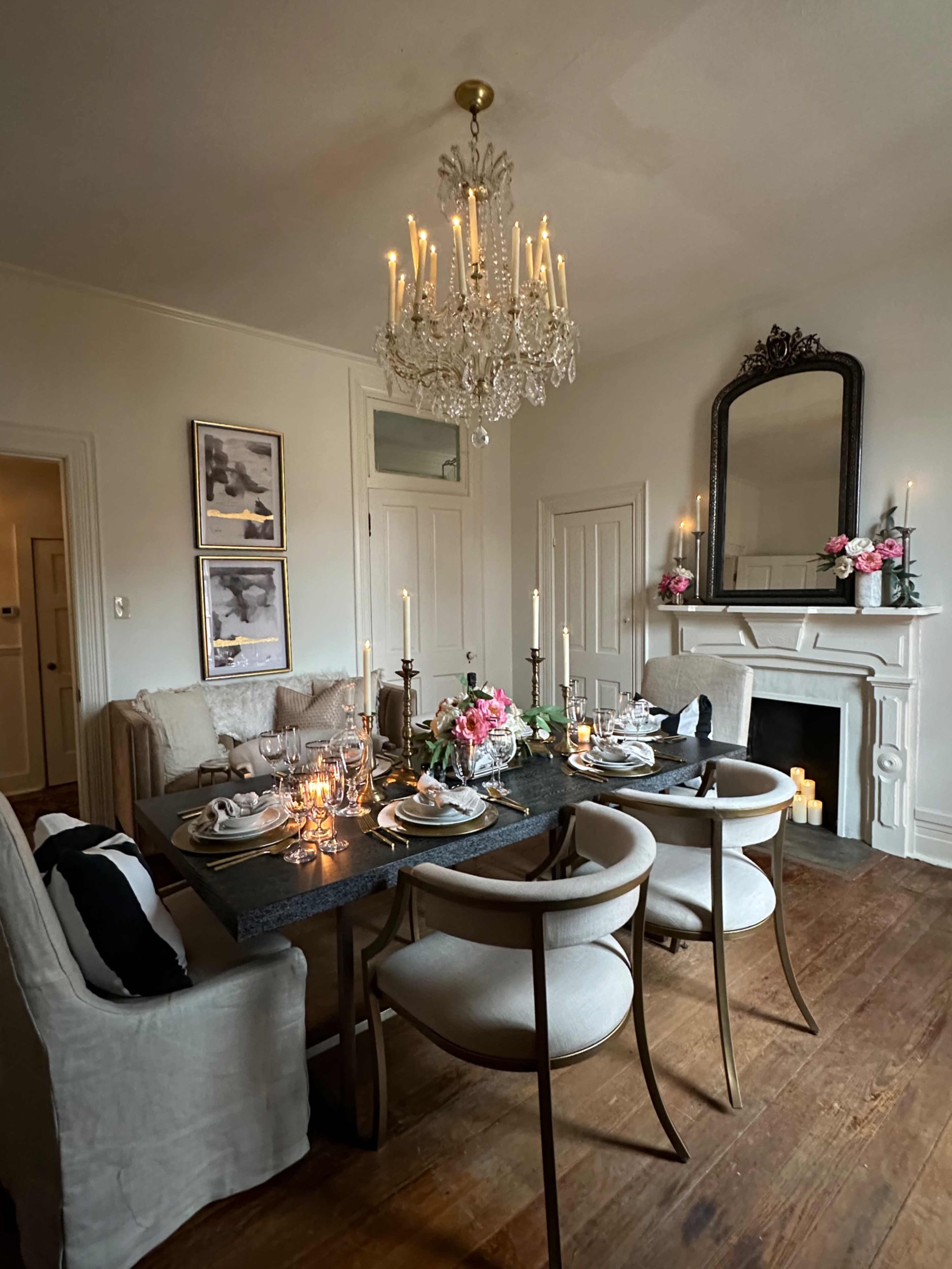 A beautifully set dining table is positioned in a well-decorated room featuring a chandelier, a fireplace, and floral arrangements.